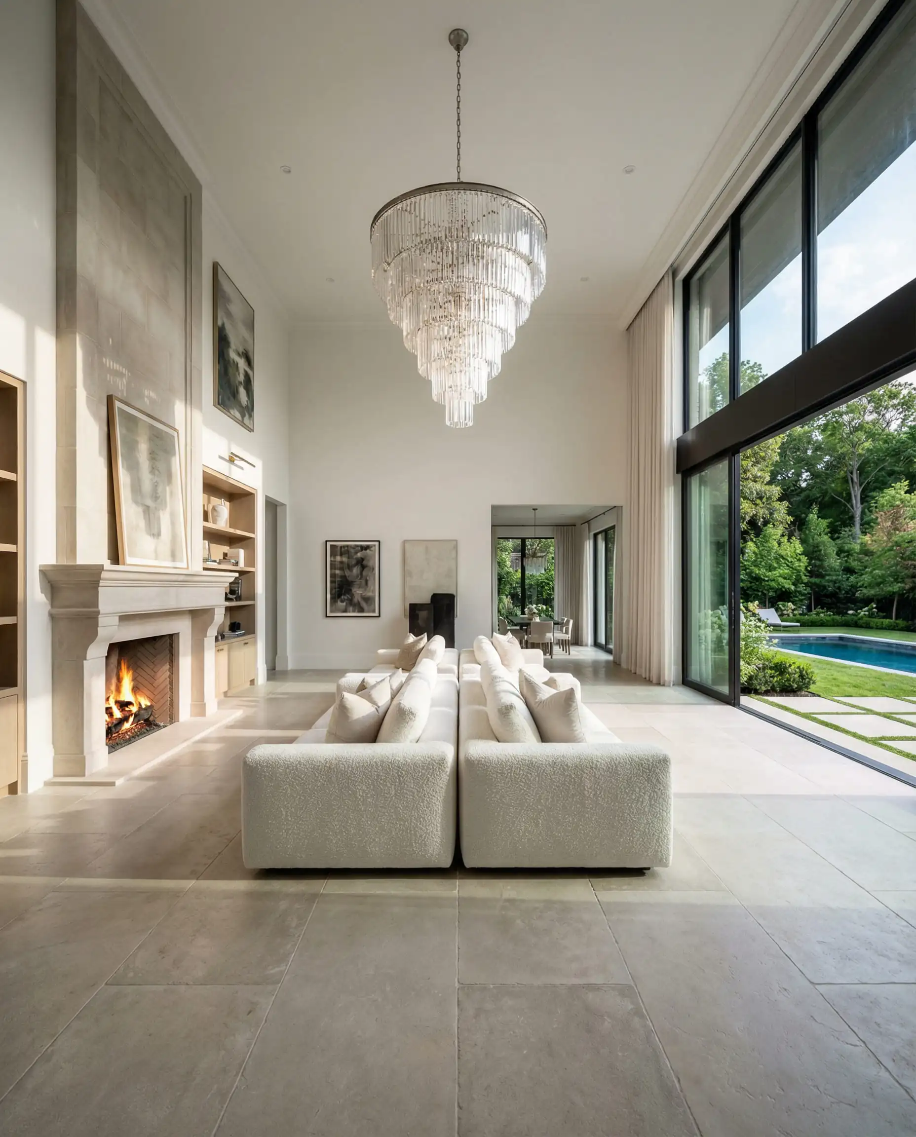 Expansive luxury living room with two white sofas placed back-to-back, one facing a fireplace and the other facing a garden view.