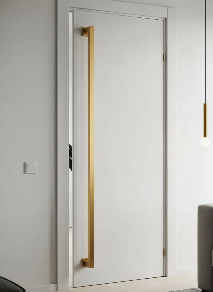 Porte à panneau plat d'un blanc éclatant, dotée d'une poignée verticale surdimensionnée sur toute la hauteur, en or mat/laiton brossé.