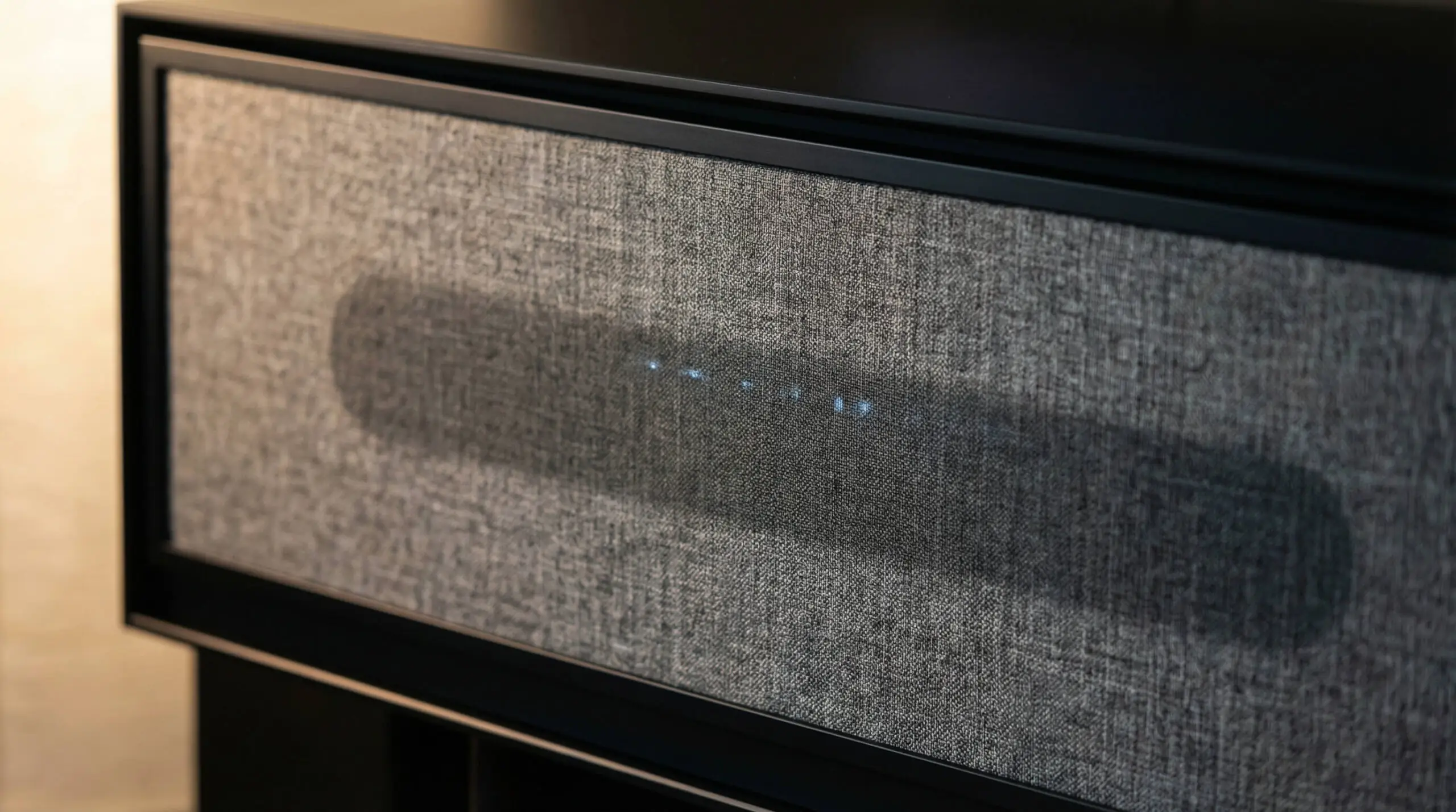 Close-up of grey acoustic speaker fabric on a media cabinet door, designed to hide soundbars while allowing audio to pass.