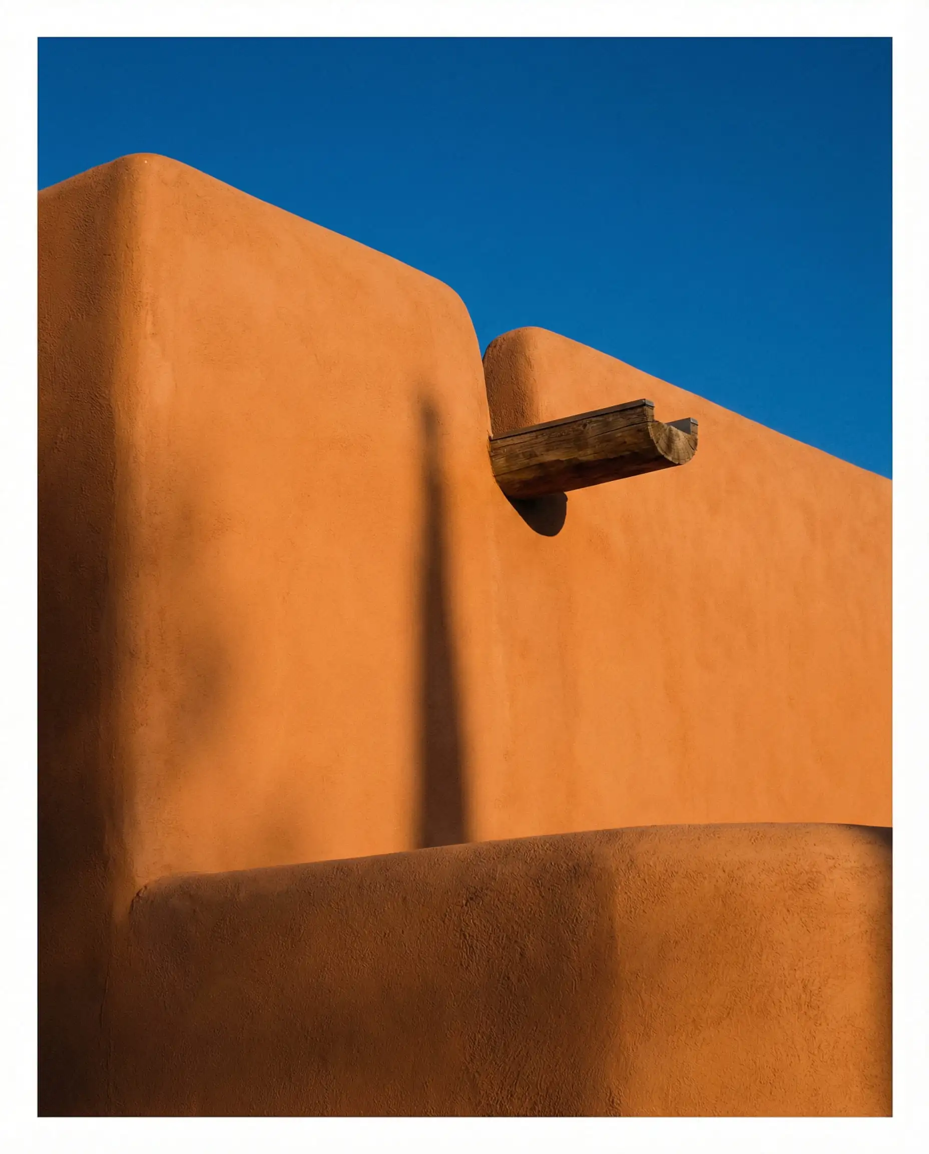 A minimalist Adobe home painted in warm Cavern Clay paint against a blue sky, showing hand-troweled texture.