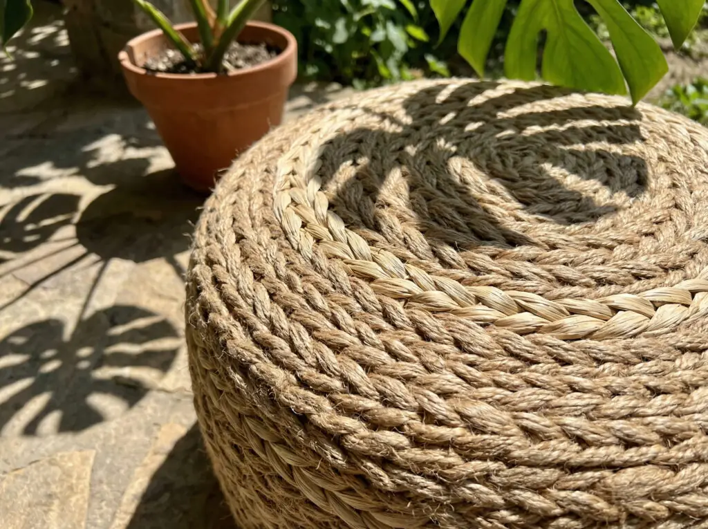 Gros plan sur un pouf rond fabriqué à partir d'épaisses fibres de jute naturelles tressées, révélant la finesse du tissage et la texture sous la lumière naturelle du soleil.