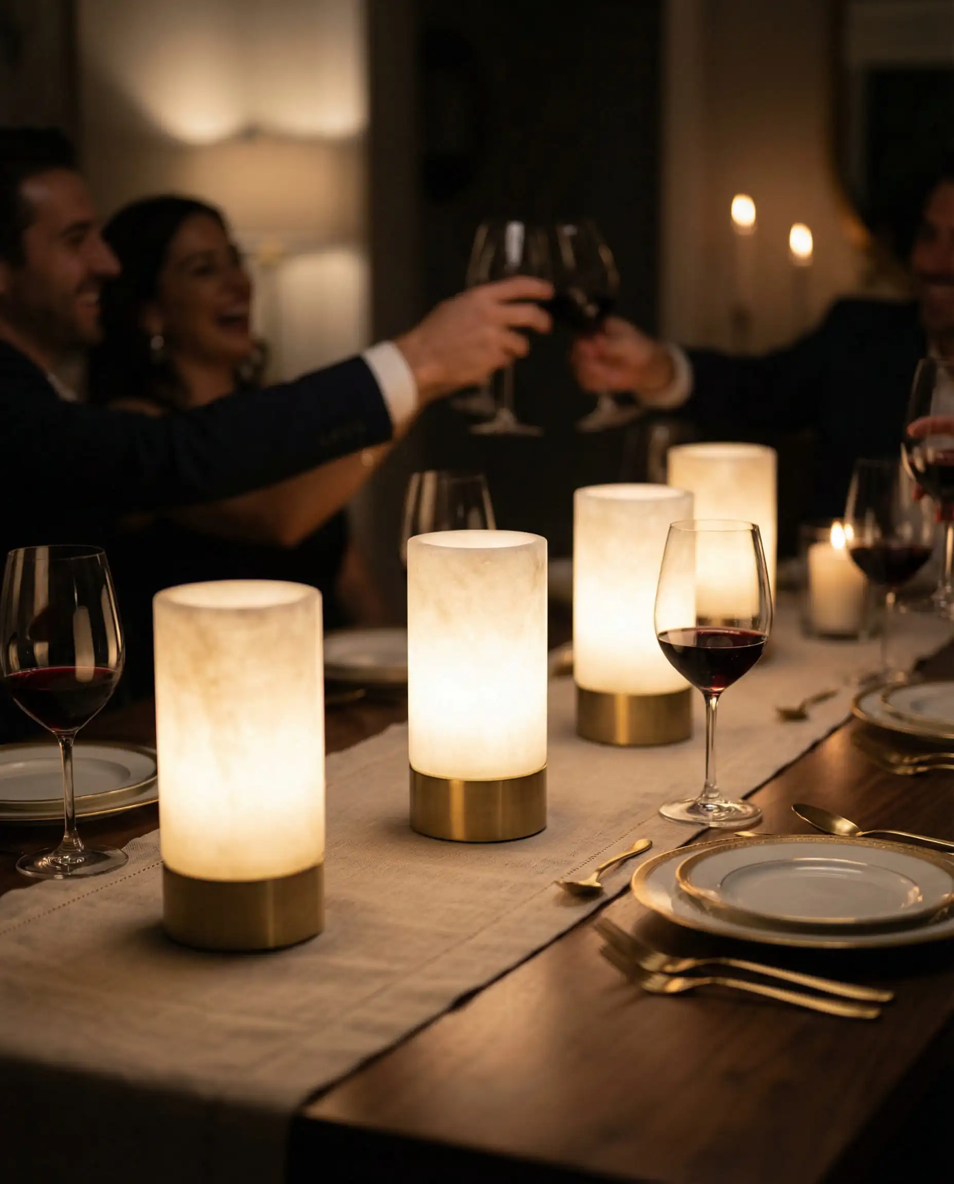 Three luxury cordless brass and alabaster table lamps styled as a centerpiece on a long walnut dining table.