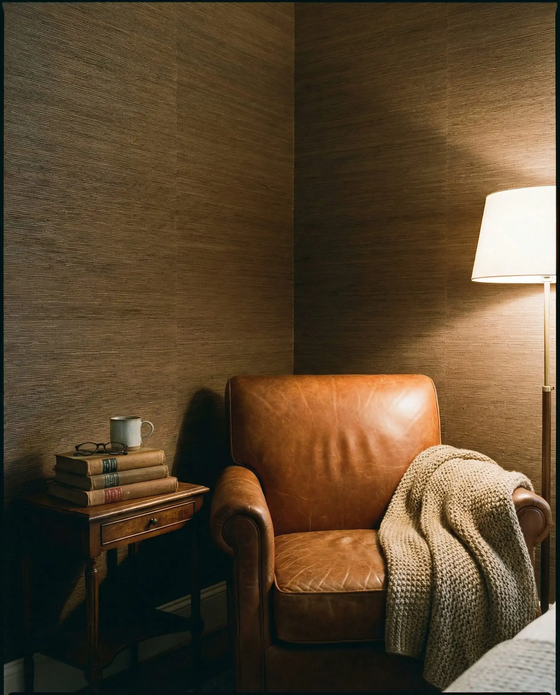 Coin chambre douillet avec papier peint en fibre végétale taupe chaud et un fauteuil en cuir.