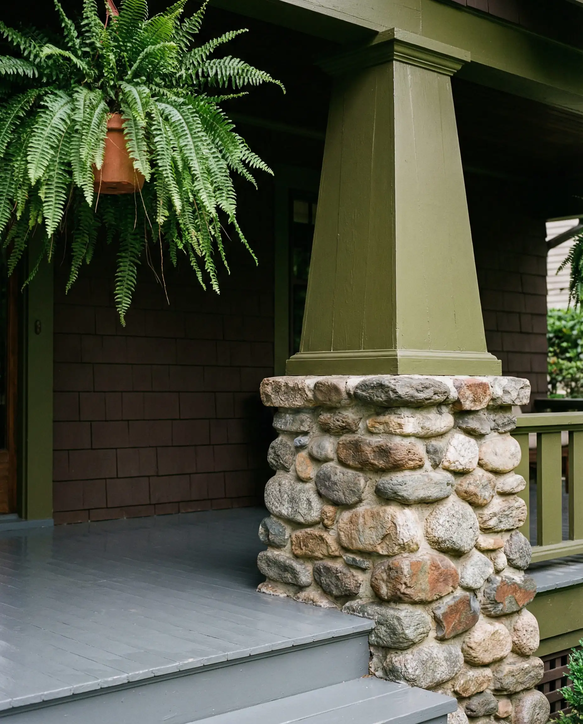 Craftsman bungalow porch details with tapered columns painted in olive green on stone piers.