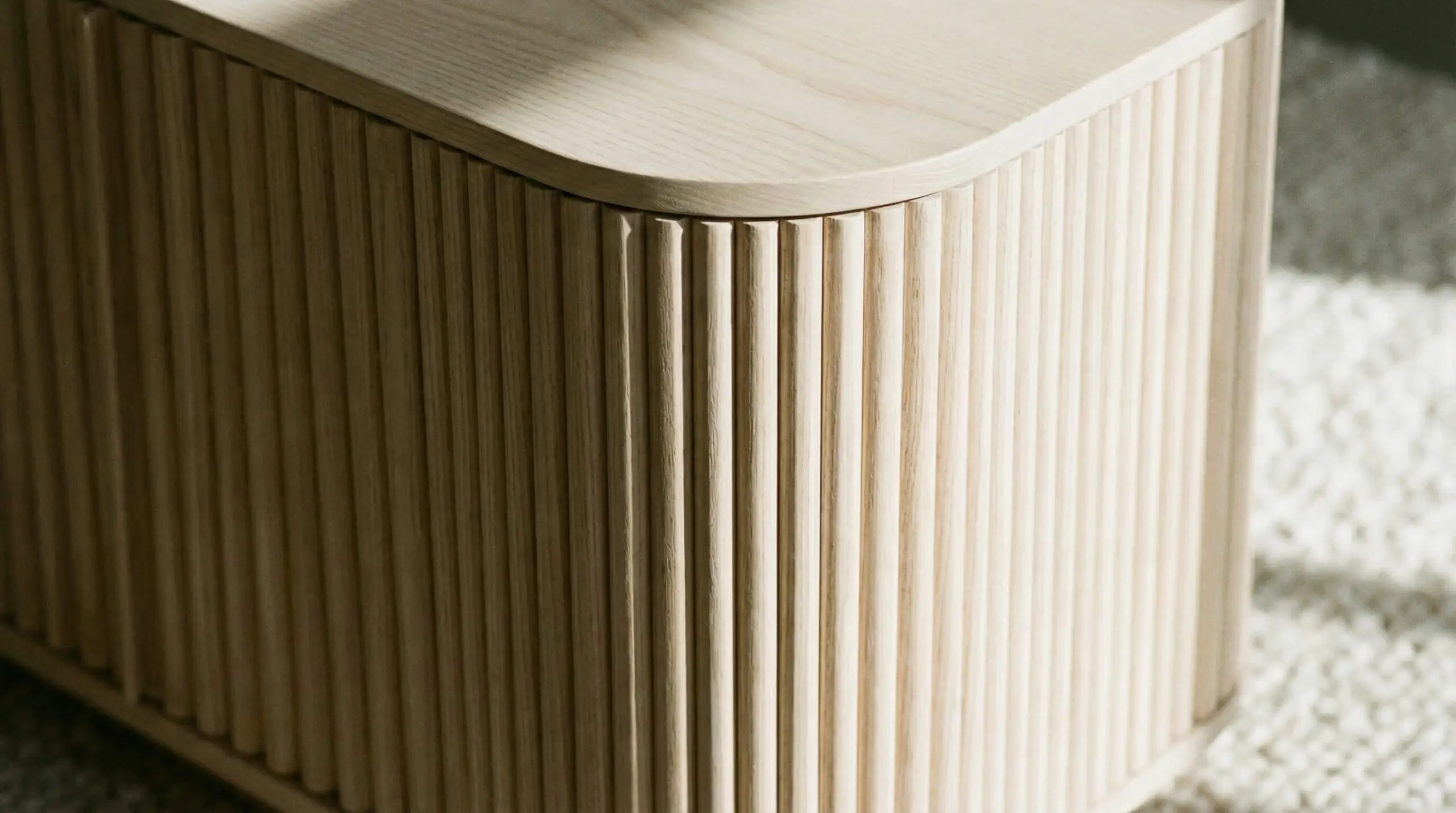 Architectural detail of vertical wood slats (fluting) wrapping seamlessly around a curved radius corner of a TV stand.