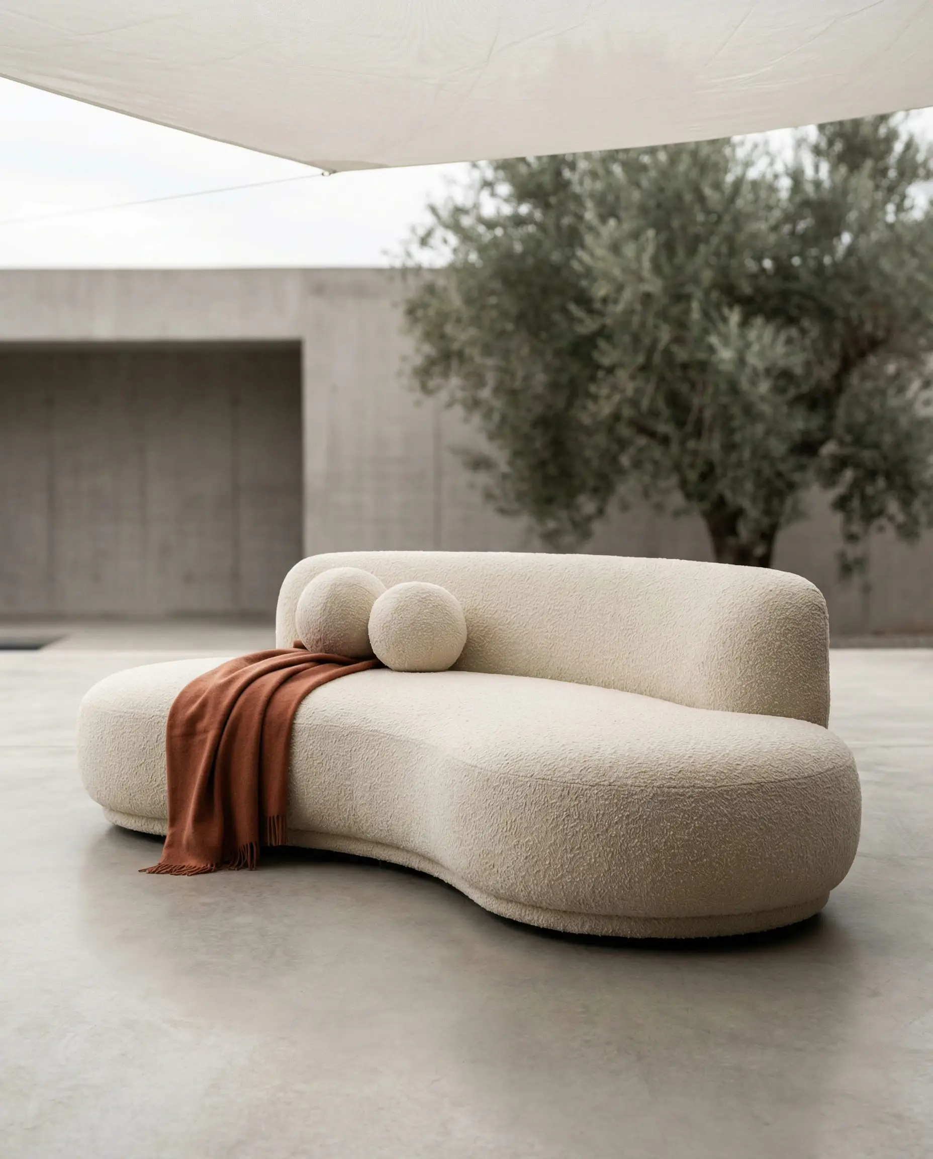 White curved outdoor sofa with boucle fabric and terracotta throw pillows on a concrete patio.