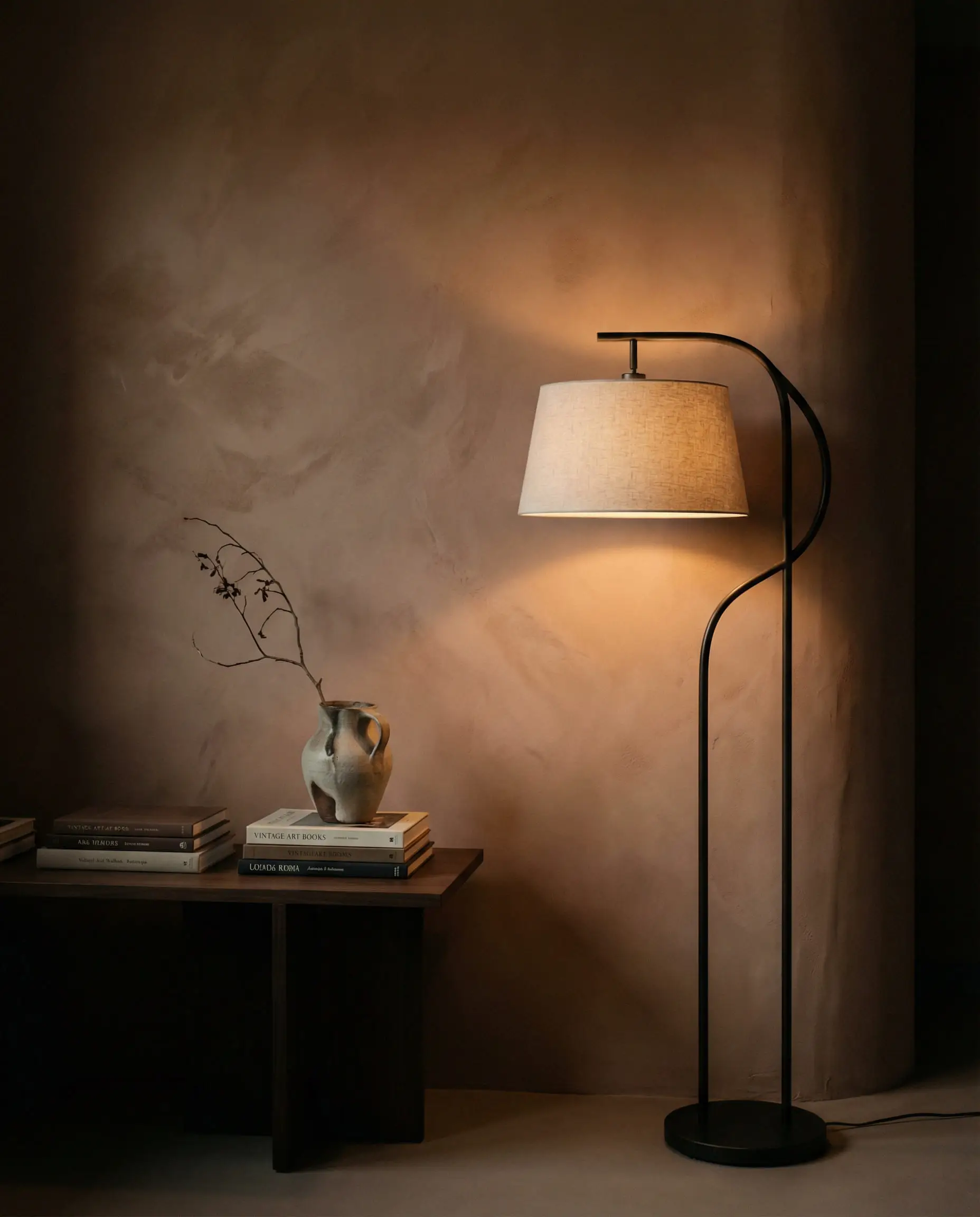 Moody living room corner with a curved wall covered in warm clay-toned plaster effect wallpaper, illuminated by a floor lamp.