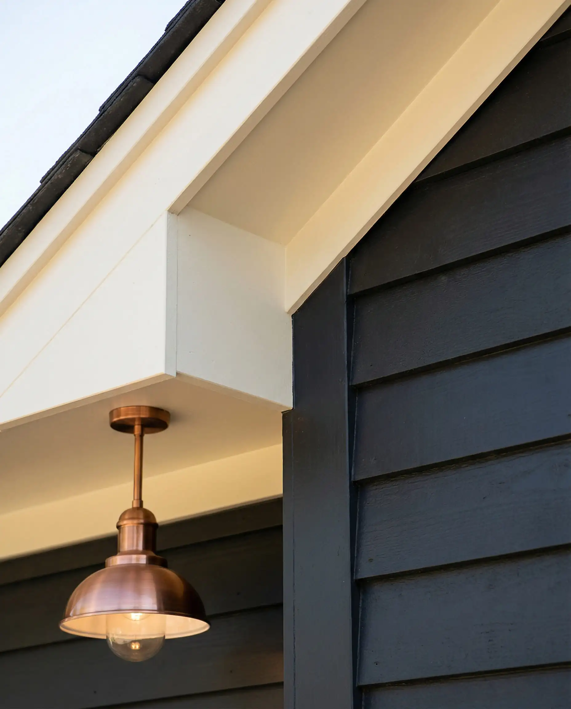 Construction detail looking up at dark charcoal siding contrasting with a bright cream painted roof soffit and fascia.