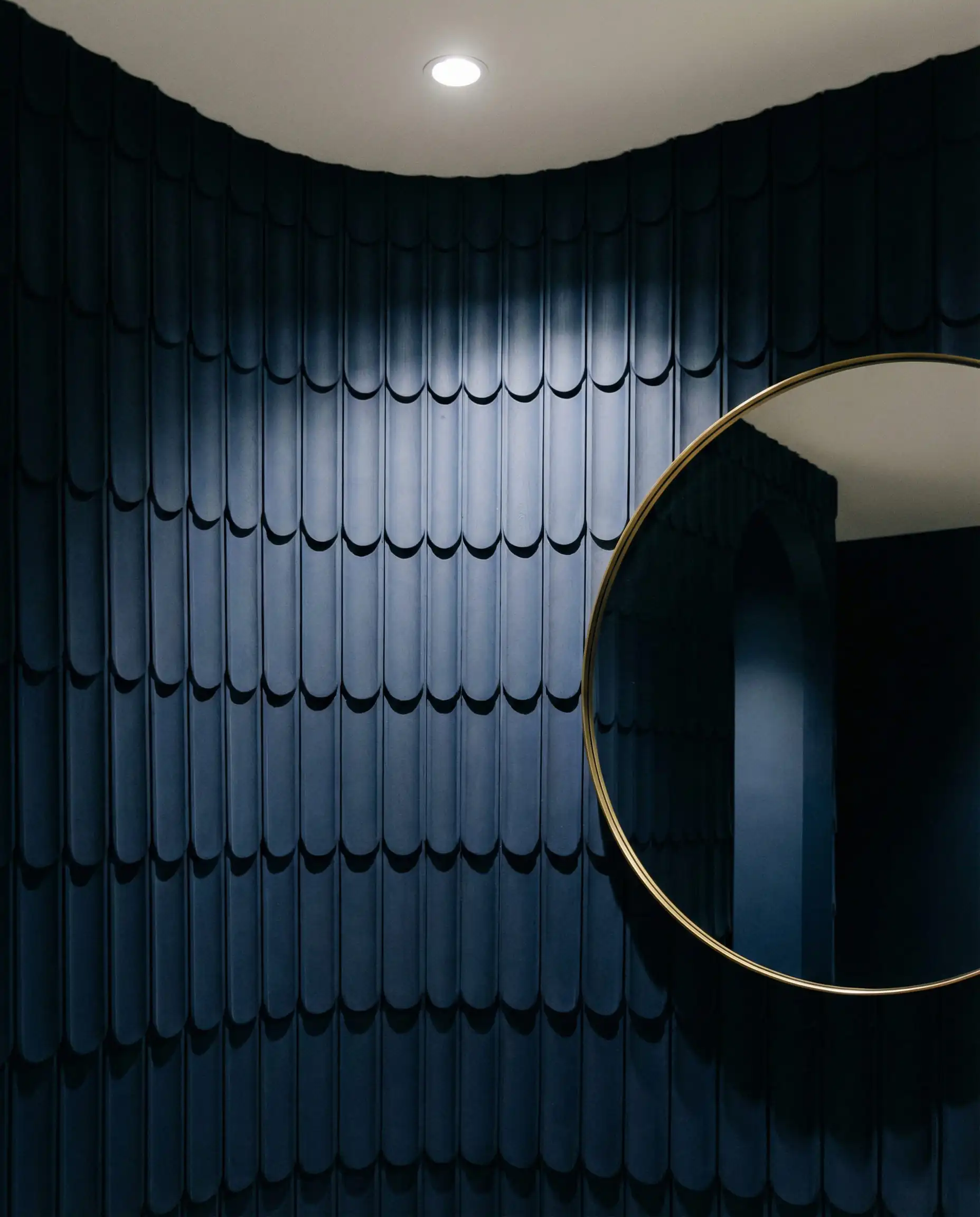 A dramatic architectural detail shot focusing on a curved wall covered in scalloped wood profiles painted in a matte, dark navy finish. This hallway features Deep matte navy, neutral white ceiling, and minimal brass detail on the mirror tones and a sculptural, abstract, high-end atmosphere.