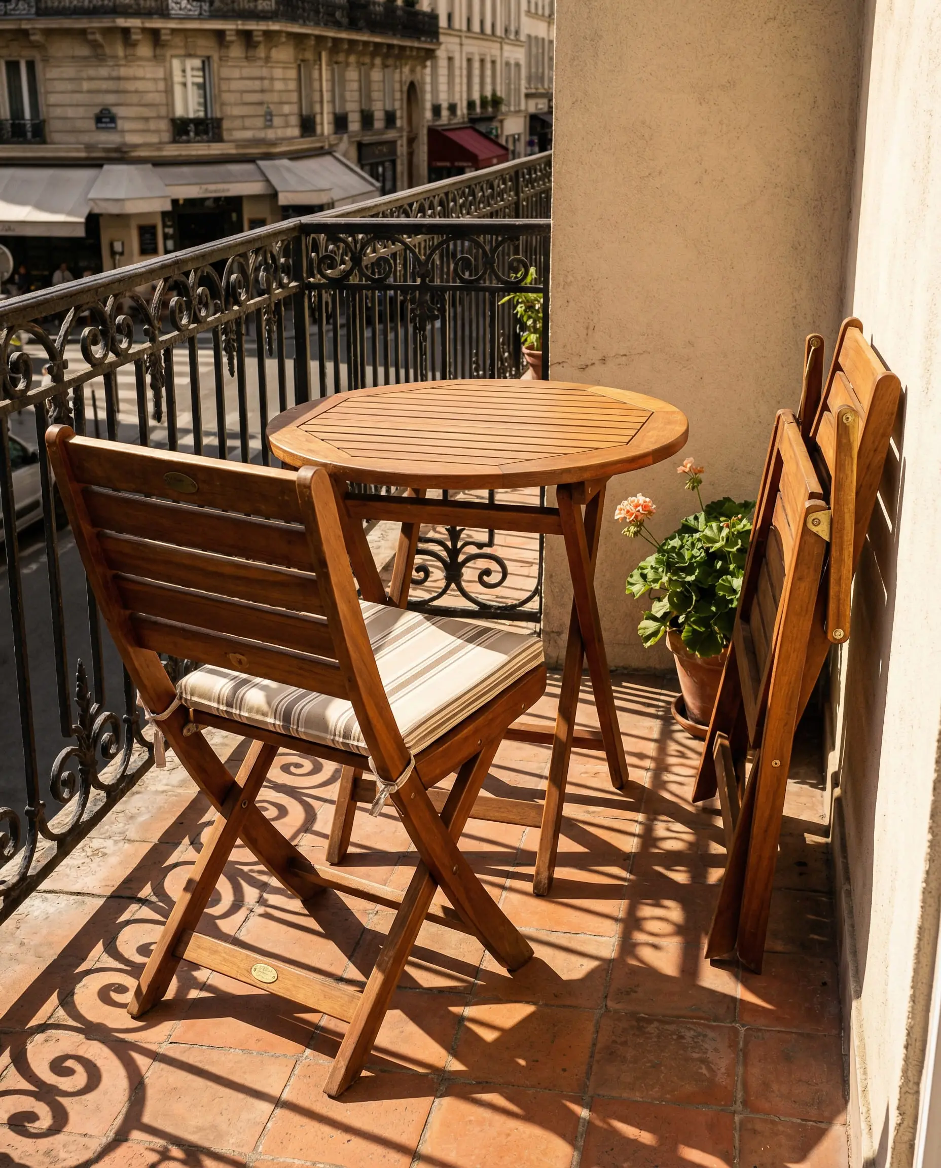 Foldable teak bistro table and chairs on a small tiled terrace.