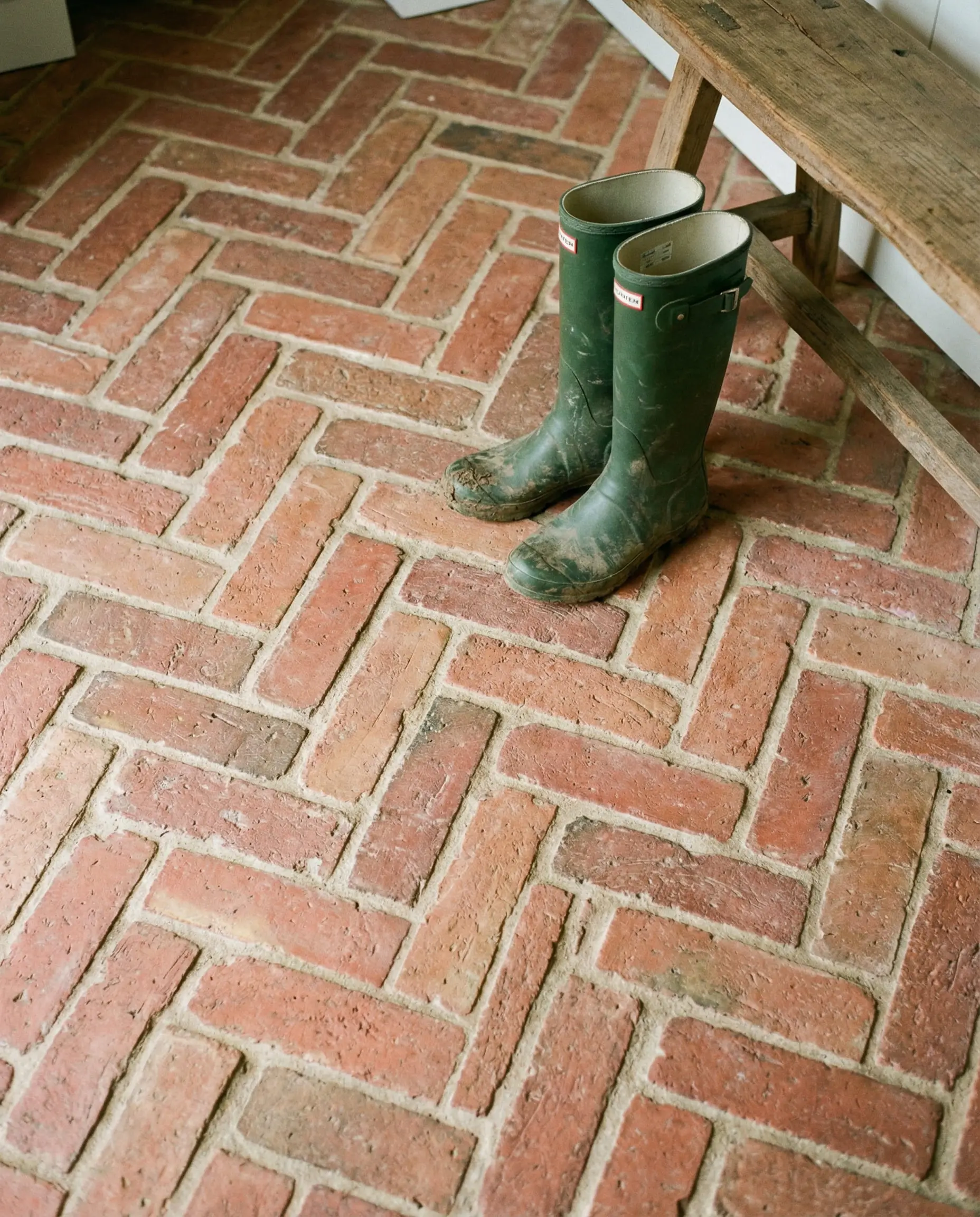 Rustic mudroom floor paved with red clay bricks in a herringbone pattern with rain boots.