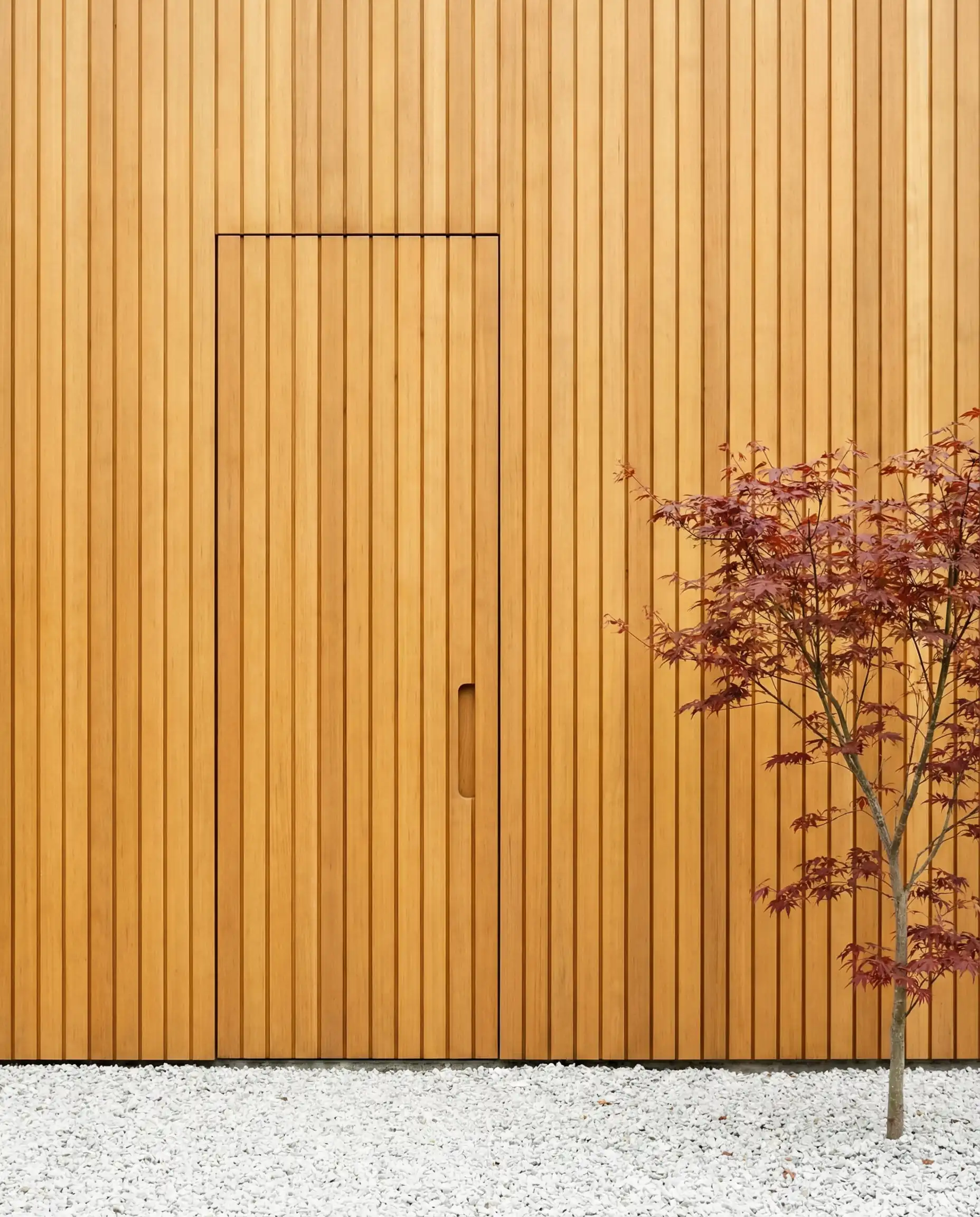 Minimalist flush front door hidden seamlessly in vertical cedar wood wall cladding.
