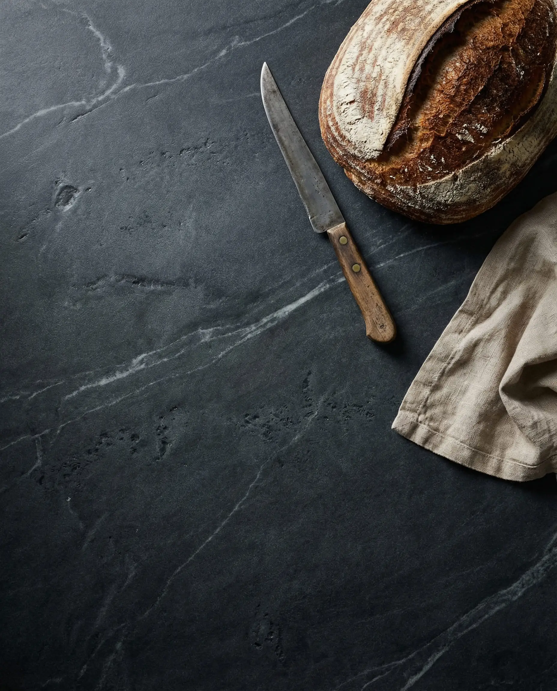 Top down view of matte honed soapstone kitchen countertop with artisan bread and vintage knife.