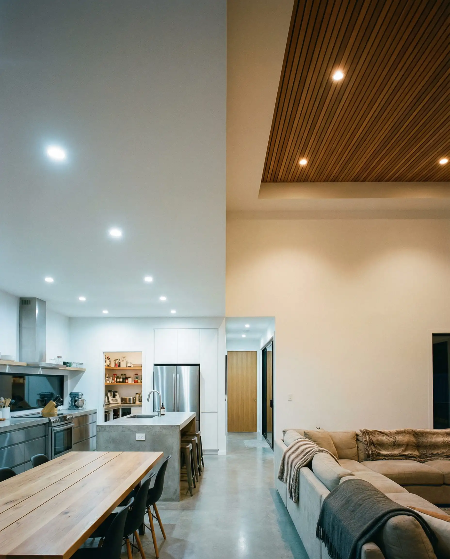 Plan large montrant la transition entre un plafond plat dans la cuisine et un plafond à lattes de bois dans le salon, dans un espace ouvert.