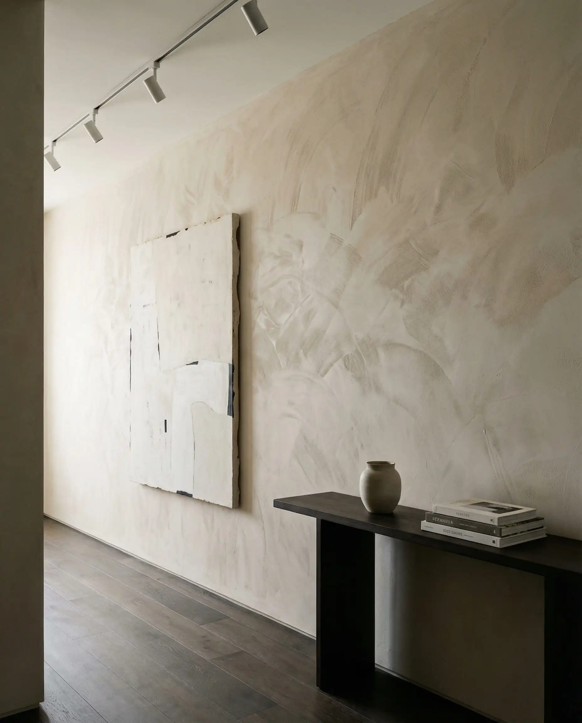 A contemporary hallway featuring a full wall of Roman clay plaster in a soft, ethereal sand color. This hallway features Soft sand, bone white, and dark wood flooring tones and a gallery-like, substantial, calming atmosphere.