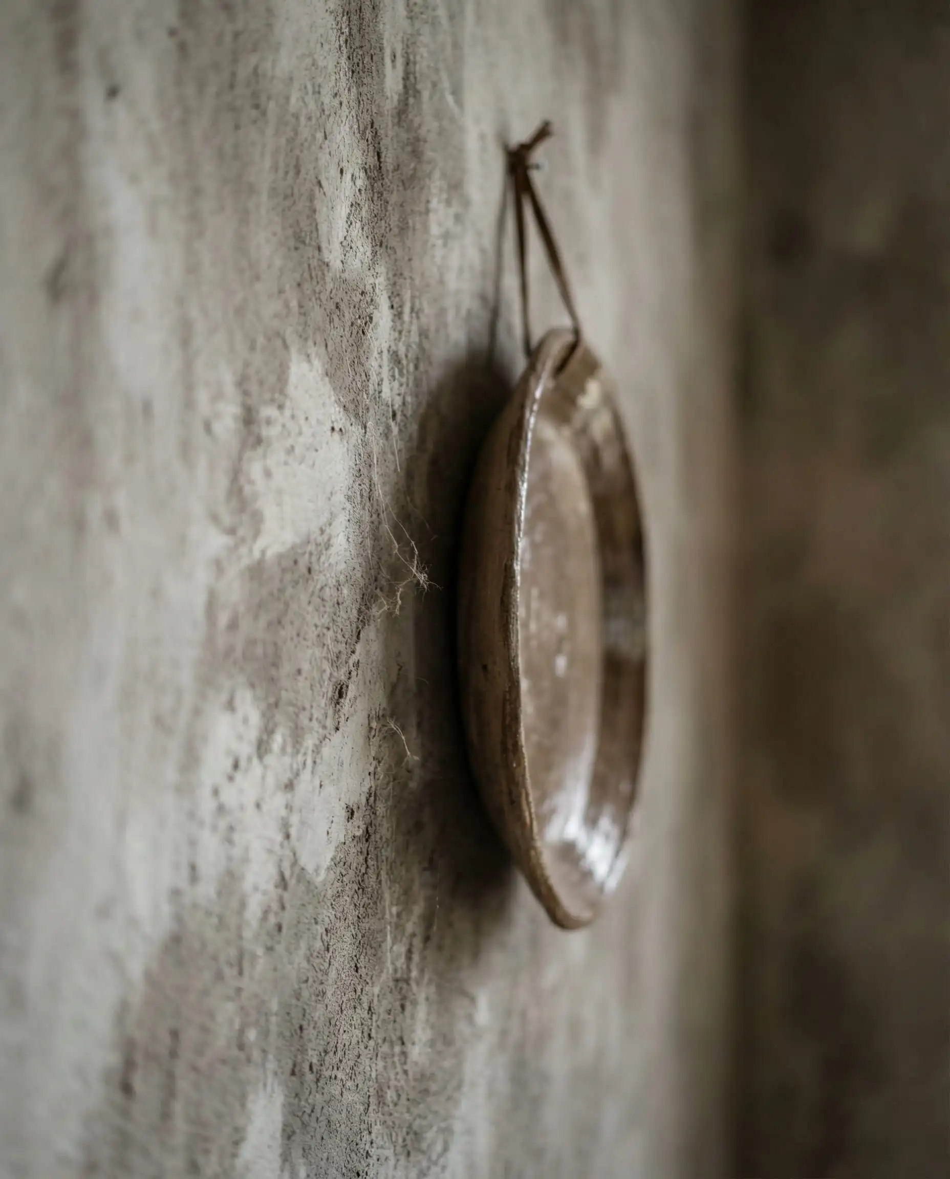 A highly textured, close-up detail of a wall finished in a two-tone limewash: a pale oyster grey applied over a subtle, darker taupe base, creating a highly mottled and historical effect. This interior features Oyster grey, dark taupe, and raw earthenware brown tones and a perfectly imperfect, historical, tactile atmosphere.