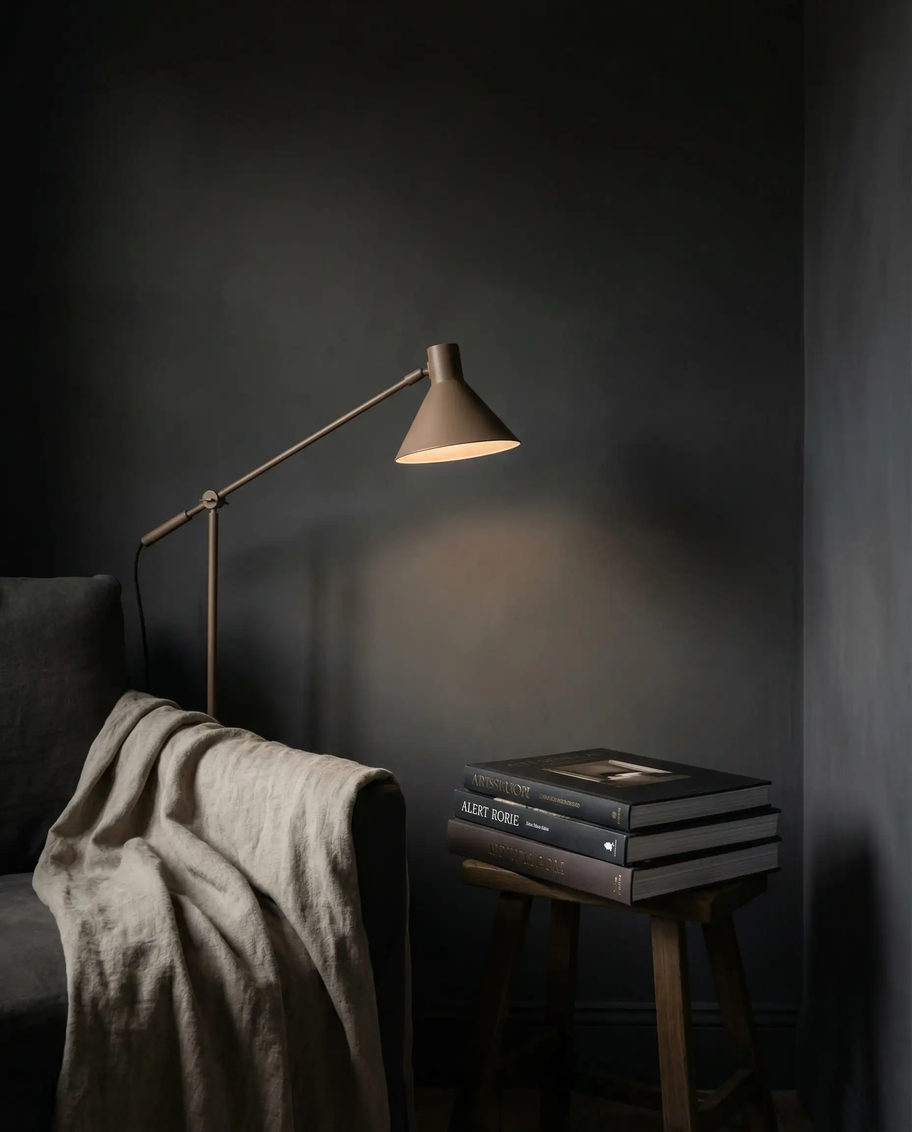 An intimate reading nook with all walls treated in a moody, deep charcoal limewash finish. This reading nook features Deep charcoal grey, soft black, and muted linen beige tones and a cocooning, introspective, quiet luxury atmosphere.