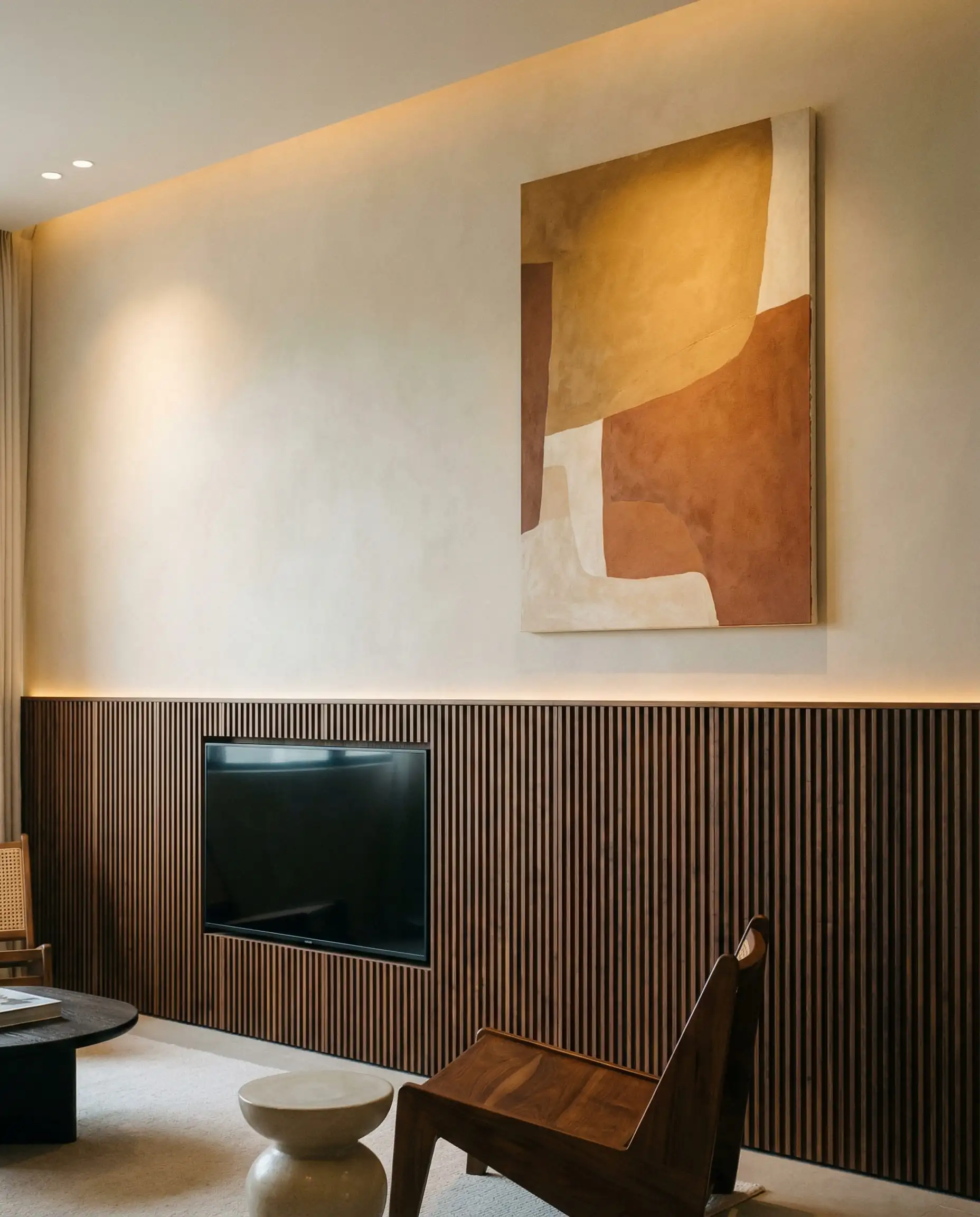 A living room wall designed with a sophisticated two-tone split. This living room features Dark walnut, soft beige, and warm ochre tones and a architectural, substantial, modern atmosphere.