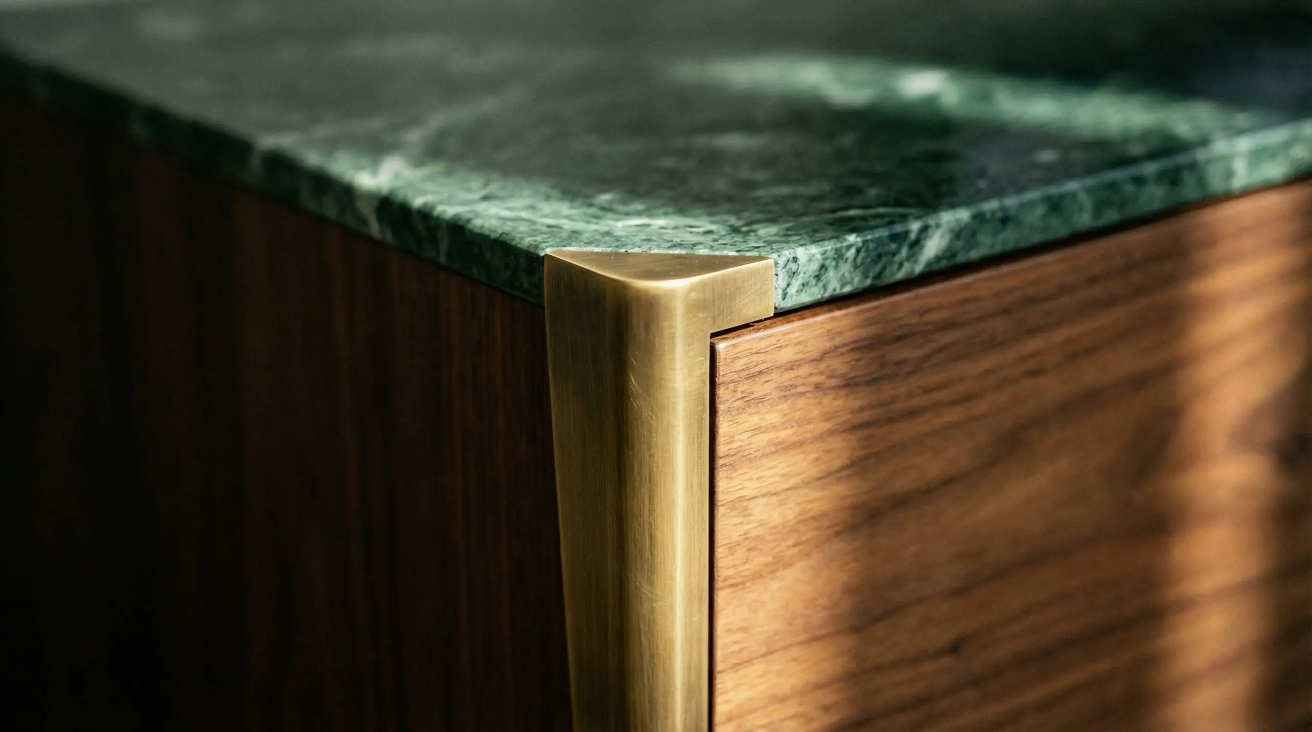 Macro detail of a media console corner showing the intersection of green marble, walnut wood, and antique brass leg.