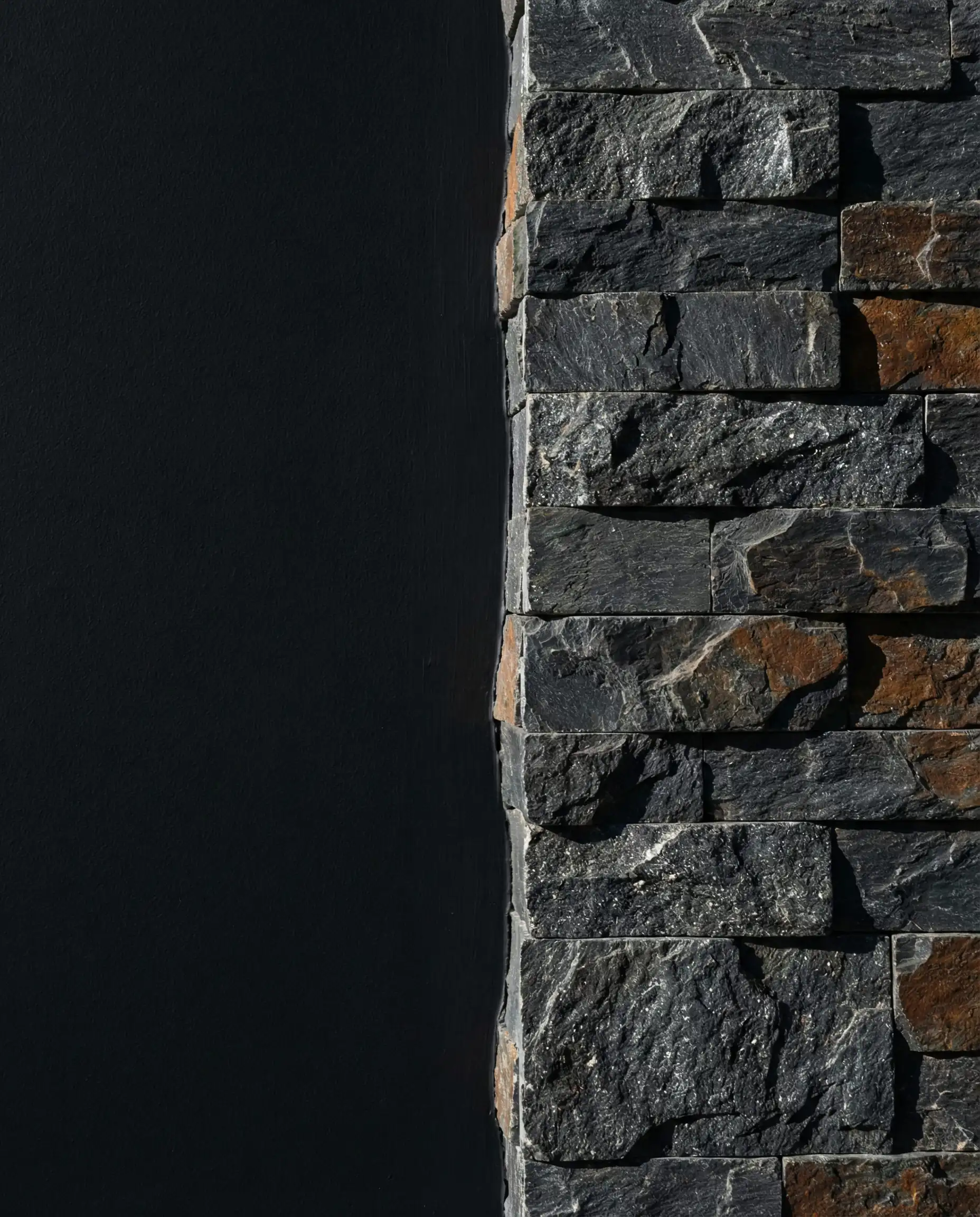 Abstract detail showing the contrast between smooth matte black painted wall and rough grey stone texture.
