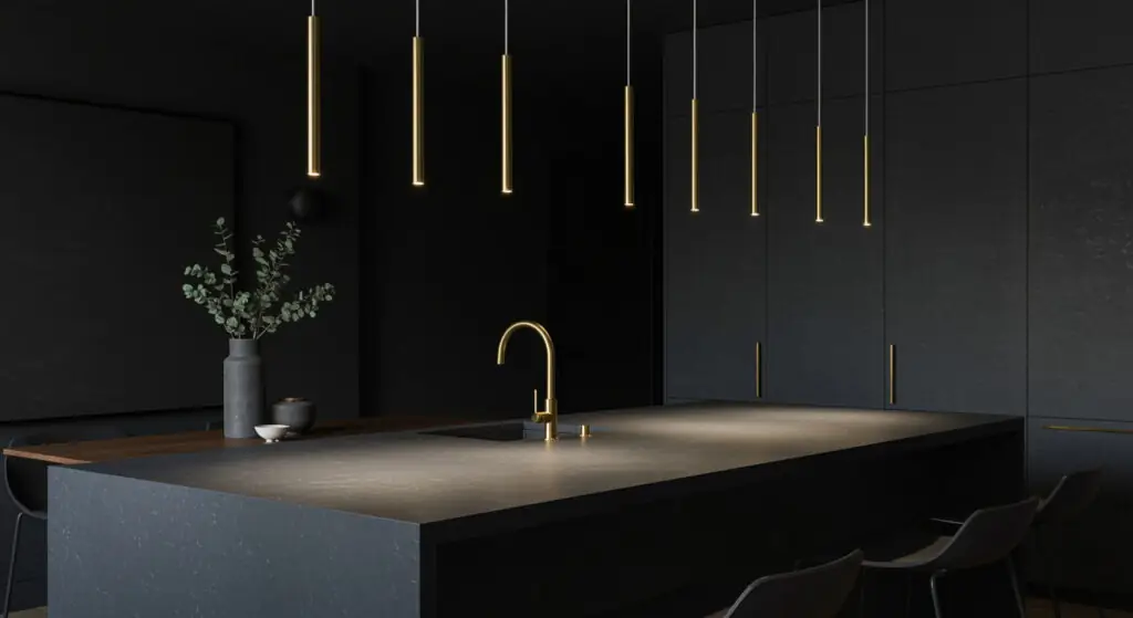 De minuscules suspensions délicates en satin doré surplombent un imposant îlot de cuisine en stéatite gris foncé, dans un décor minimaliste.