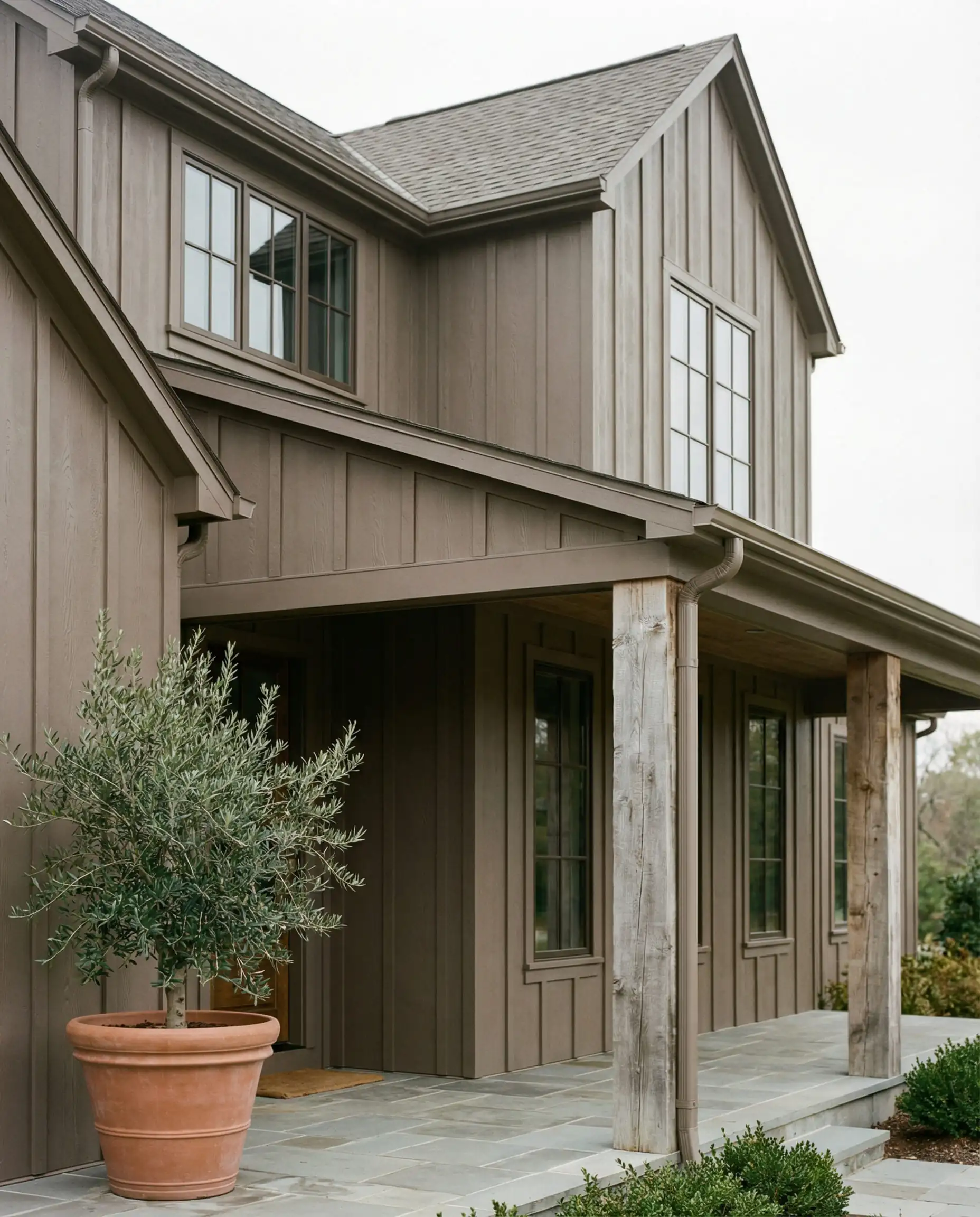 Vertical board-and-batten siding painted in a warm greige taupe color featuring bronze window frames and a reclaimed wood porch.