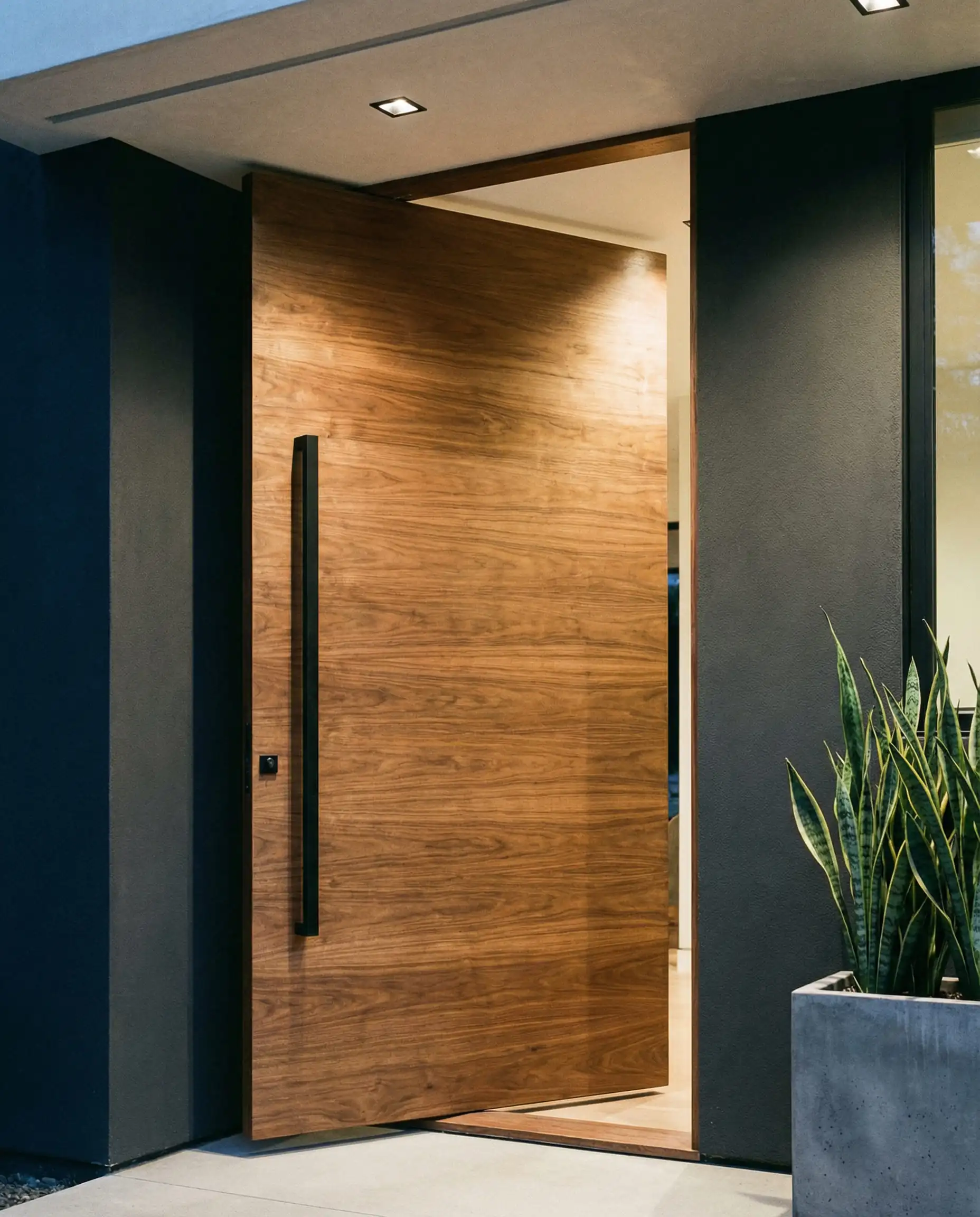 Modern entryway featuring a large natural walnut wood pivot door with black hardware.