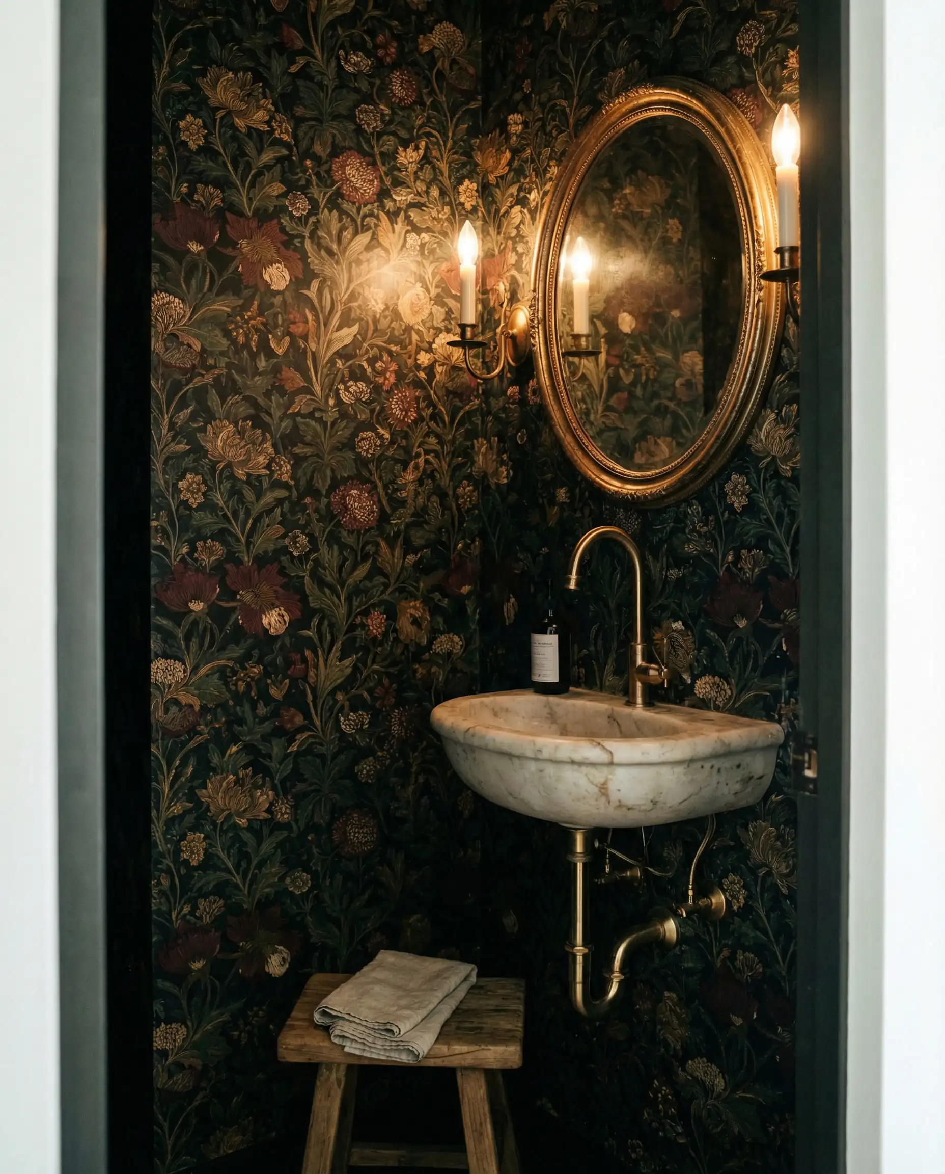 Small powder room featuring dark moody floral wallpaper and a vintage gold mirror.