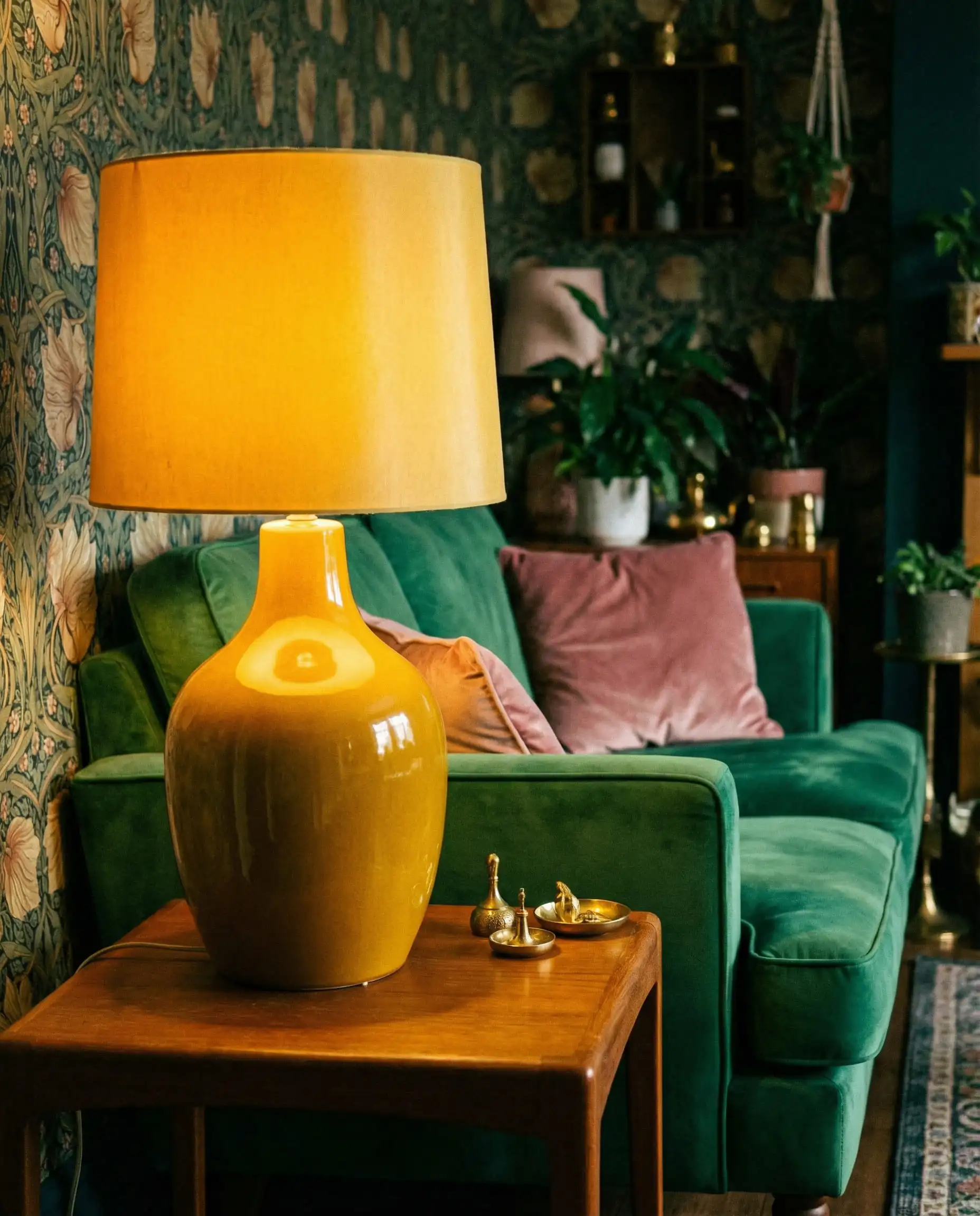 Vintage-inspired glossy mustard yellow table lamp styled in an eclectic living room with an emerald green velvet sofa.