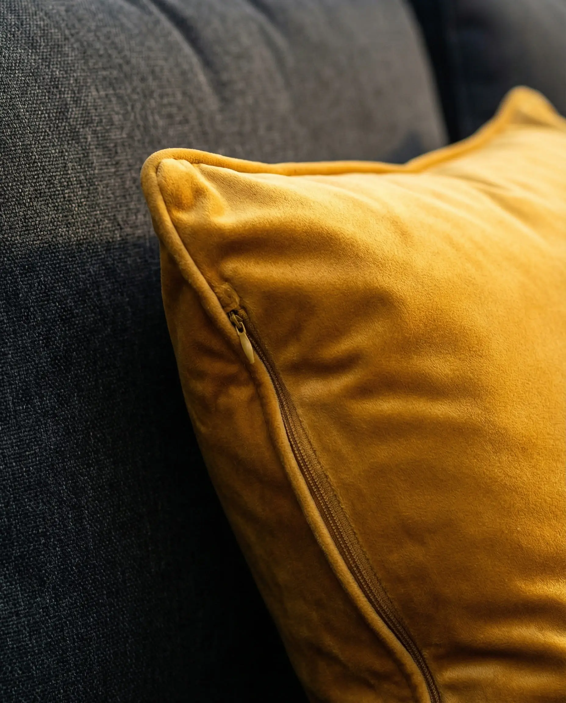 Deep ochre yellow velvet throw pillow on a dark charcoal outdoor sofa.