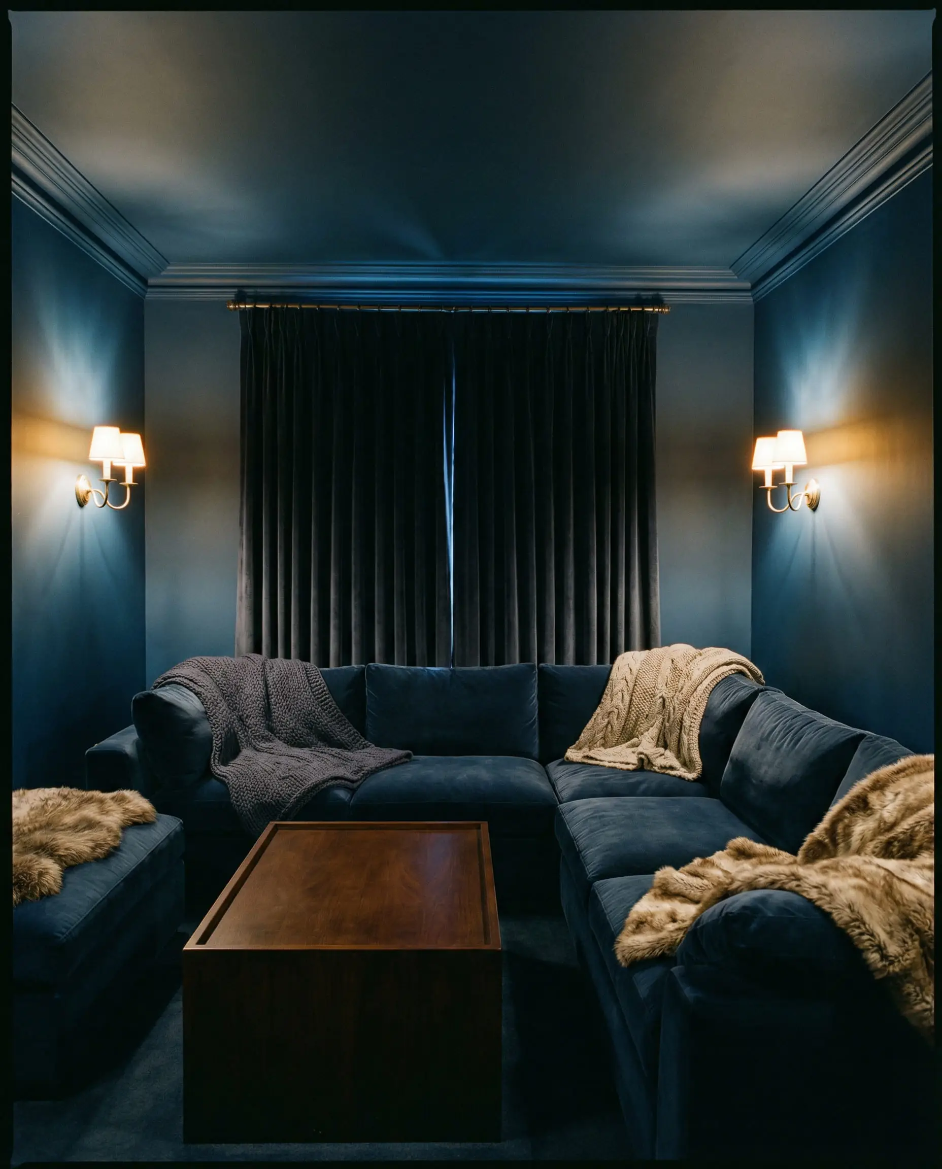 Cozy enclosed media room painted entirely in navy blue with velvet sofa and brass sconces.