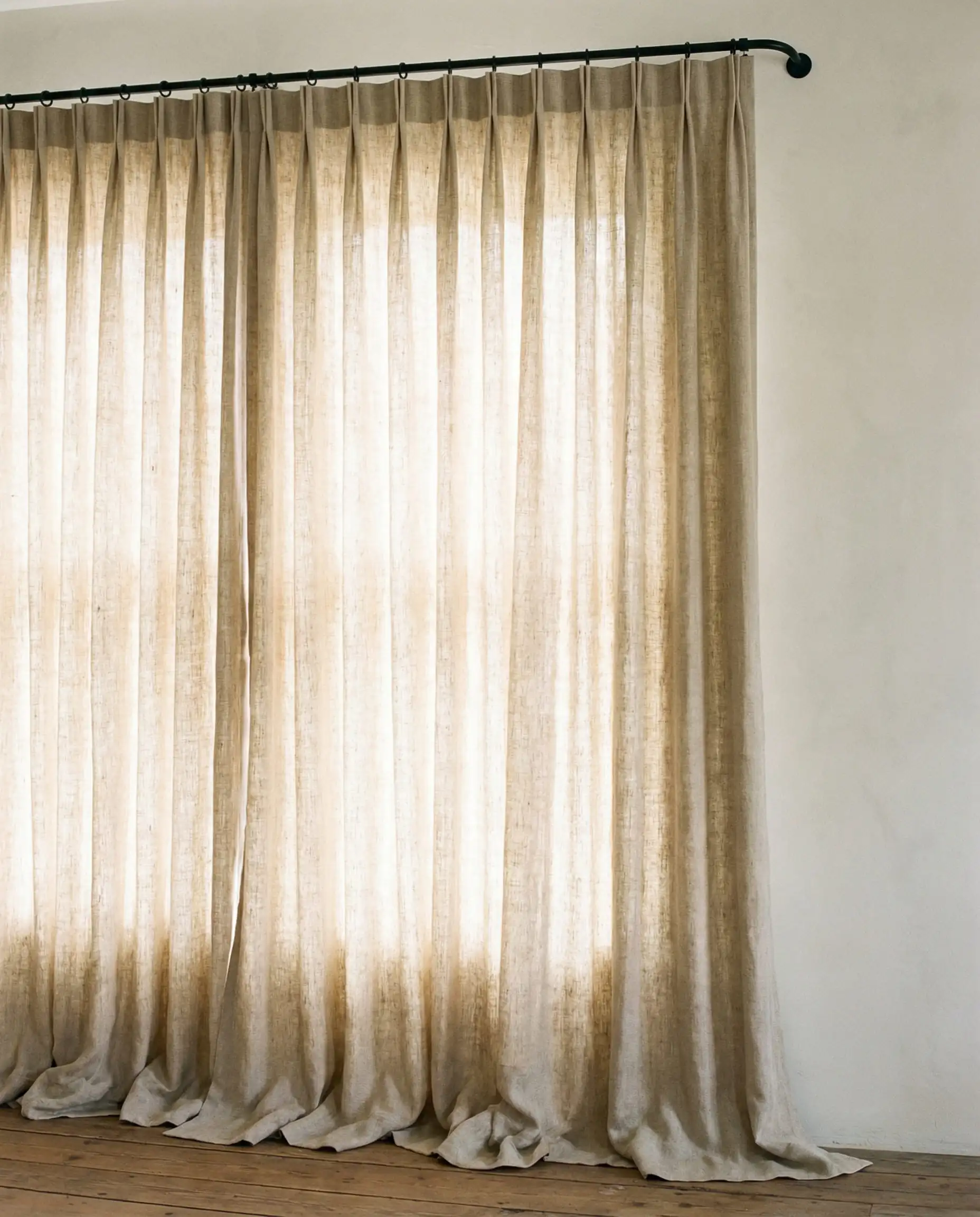 Floor to ceiling oatmeal linen pinch pleat drapes puddling on a wooden floor.