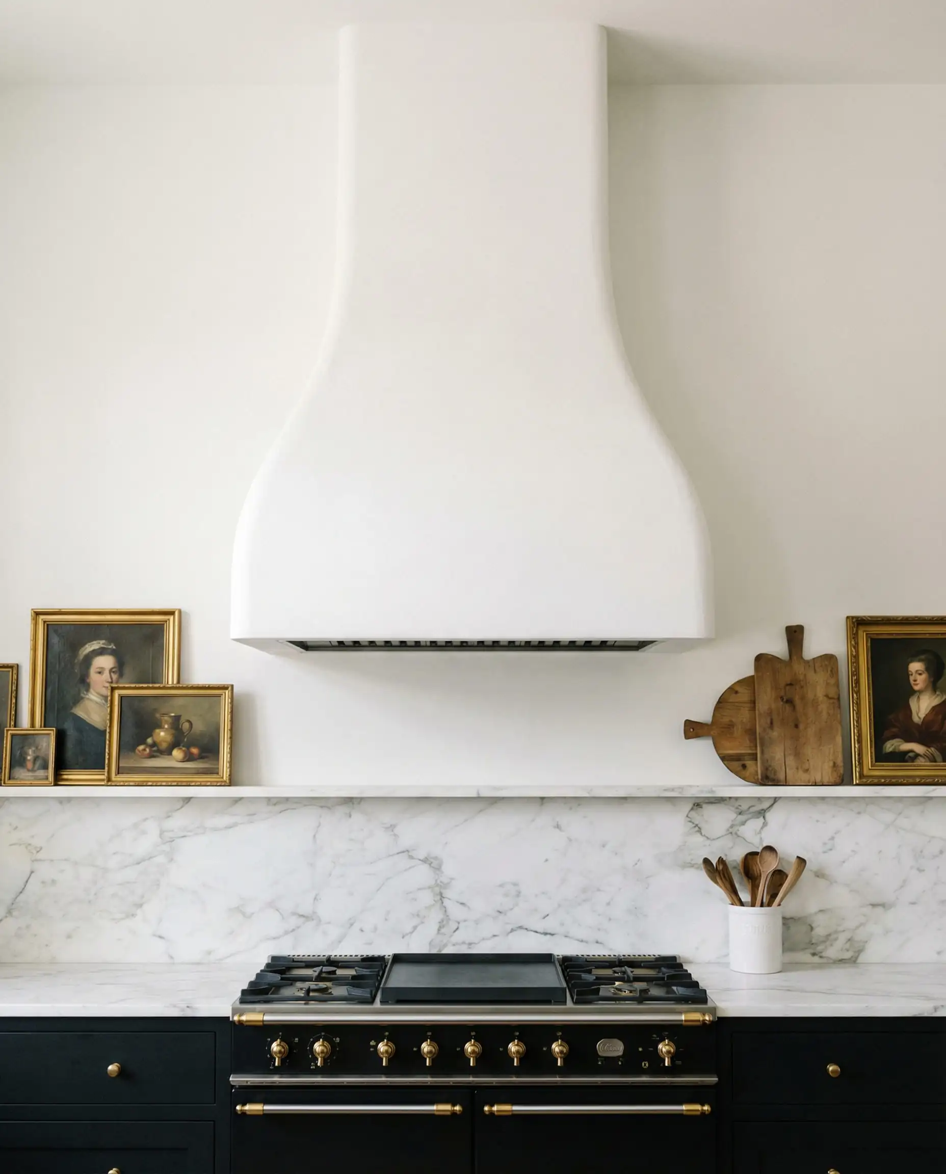 Large curved white plaster kitchen range hood over a black professional range cooker with marble backsplash.