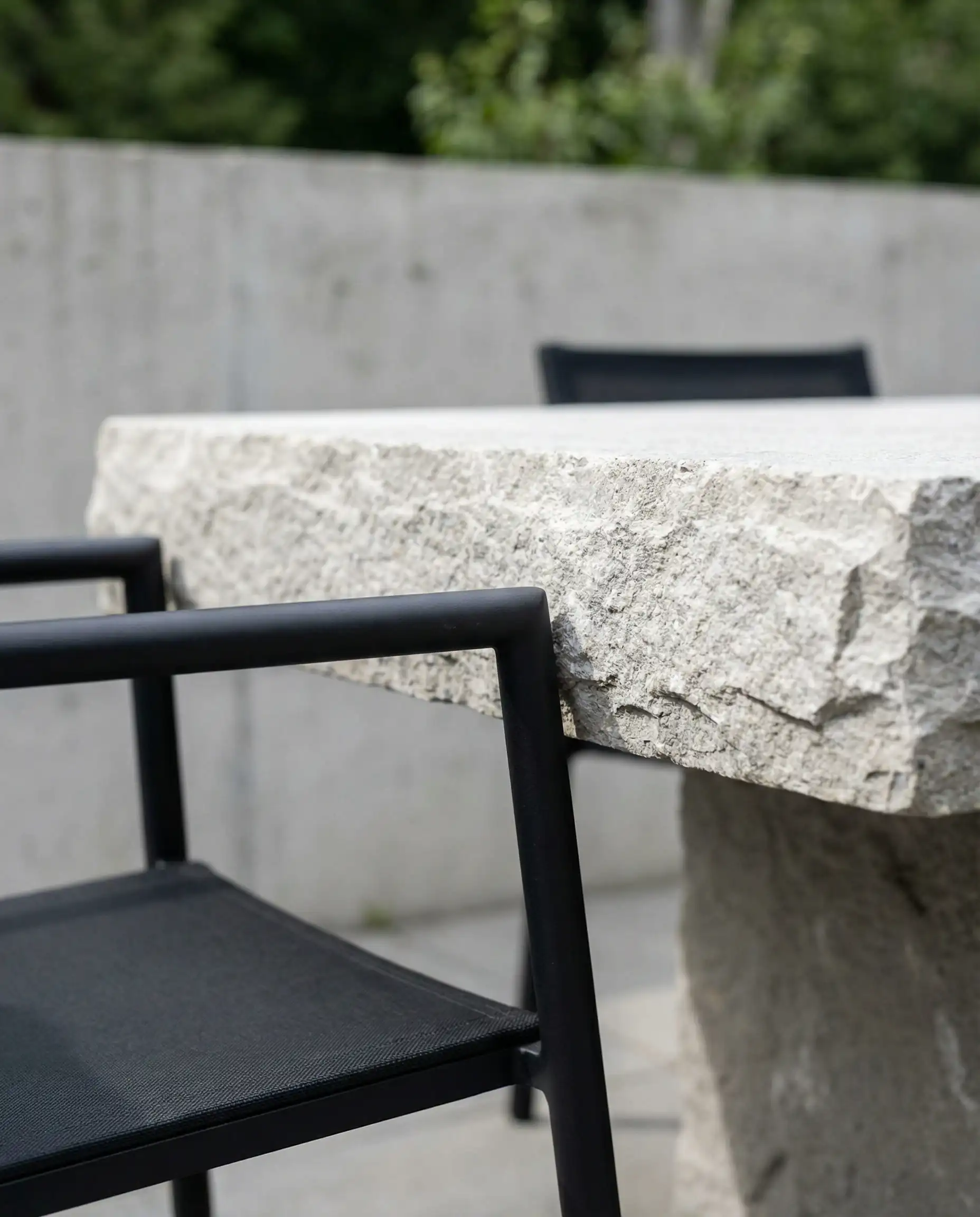 Modern black aluminum dining chair tucked into a raw stone dining table.