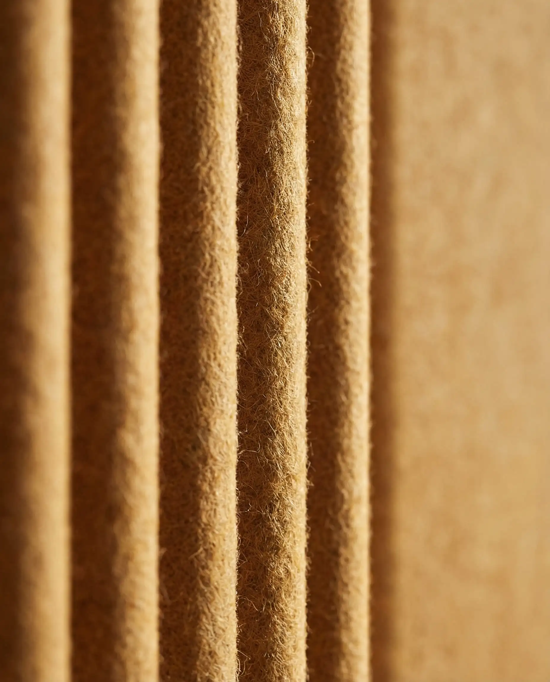 Close-up macro shot of fluted acoustic wall panels made from recycled PET felt in a warm ochre color. The image shows the soft, fibrous texture of the 3D ridges, highlighting sustainable luxury wall trends.