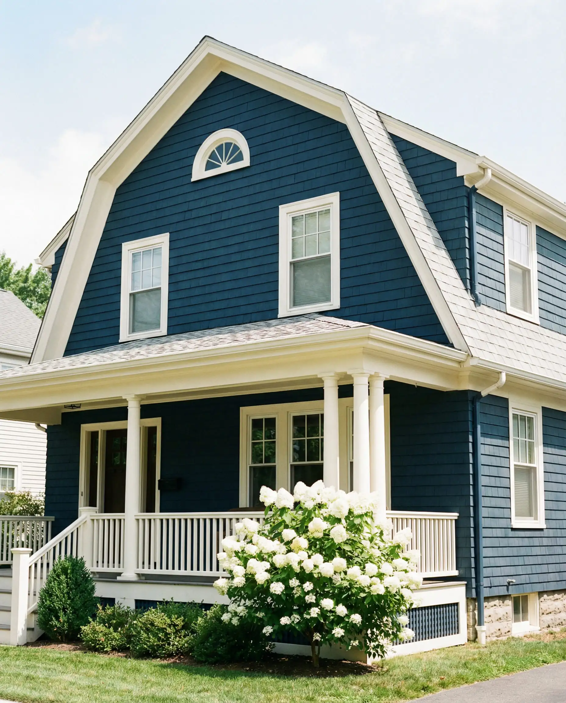 A Dutch Colonial home featuring a deep Navy Blue body with creamy white trim outlining the gambrel roof.