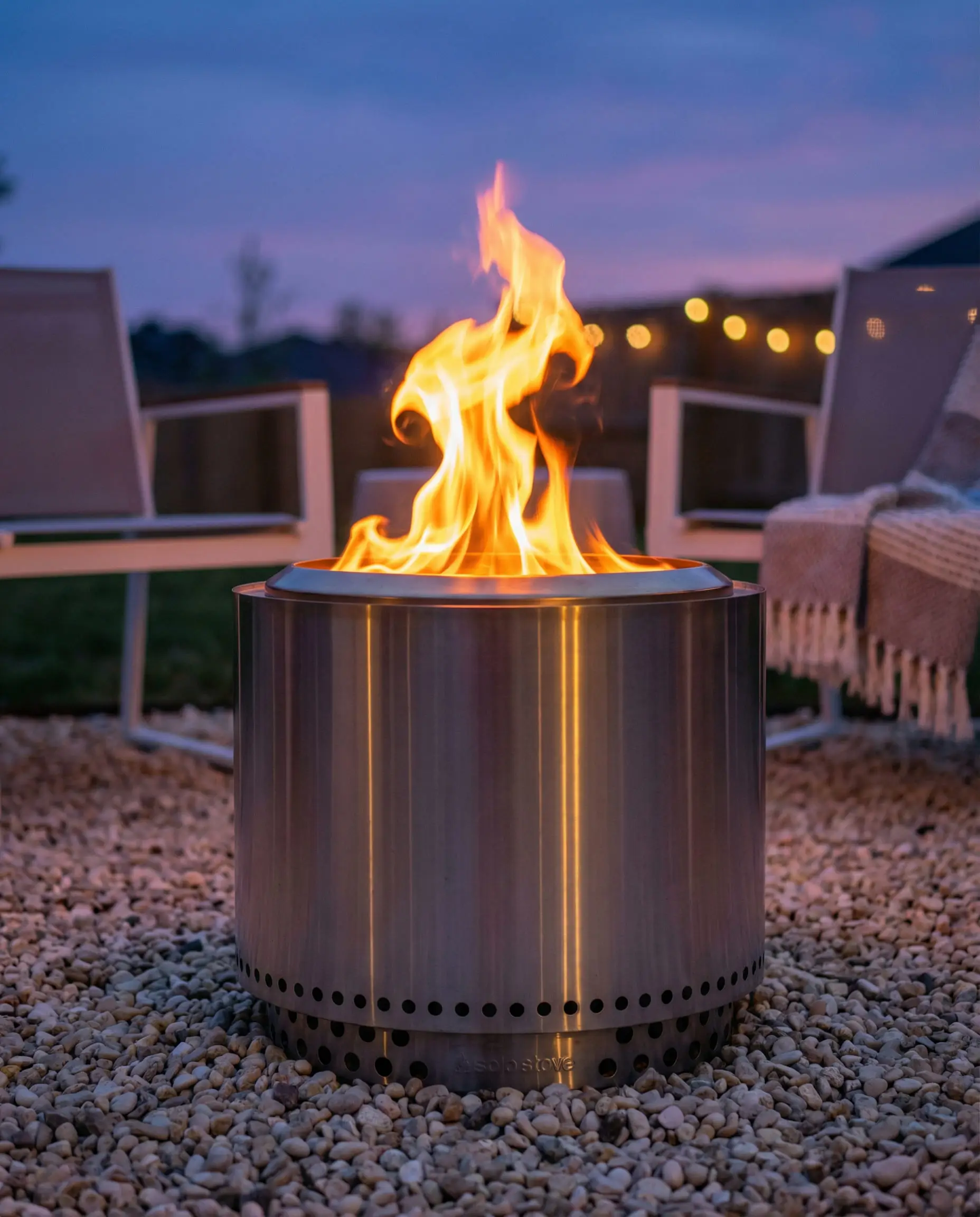 Stainless steel smokeless fire pit burning efficiently on a gravel patio at dusk.