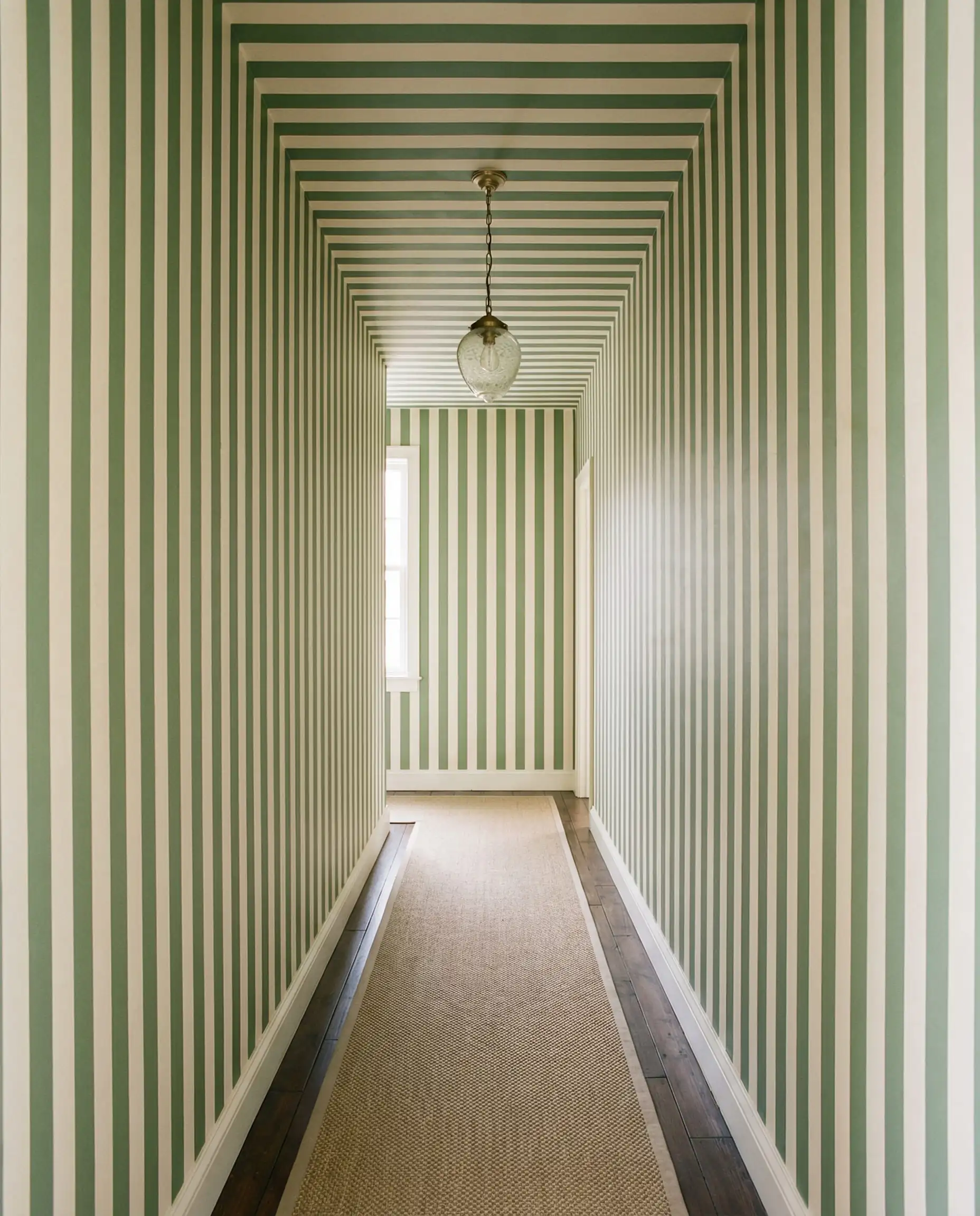 Couloir étroit avec papier peint à rayures verticales se prolongeant sans couture sur le plafond.