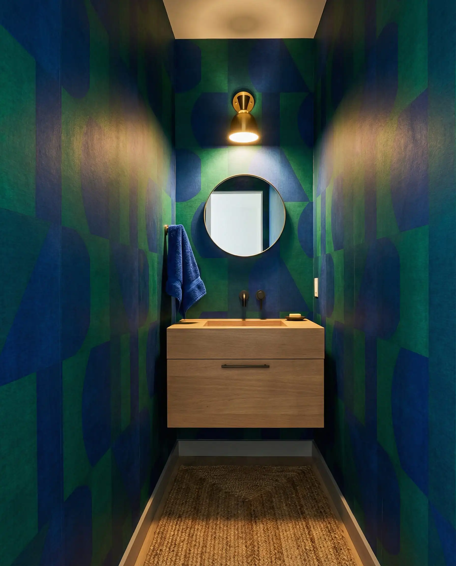 A chic powder room where the walls are wrapped in a high-performance, PVC-free vinyl alternative wallpaper featuring a large-scale, geometric print in deep, saturated jewel tones. This powder room features Deep sapphire blue, emerald green, and light oak tones and a bold, sustainable luxury, jewel box atmosphere.