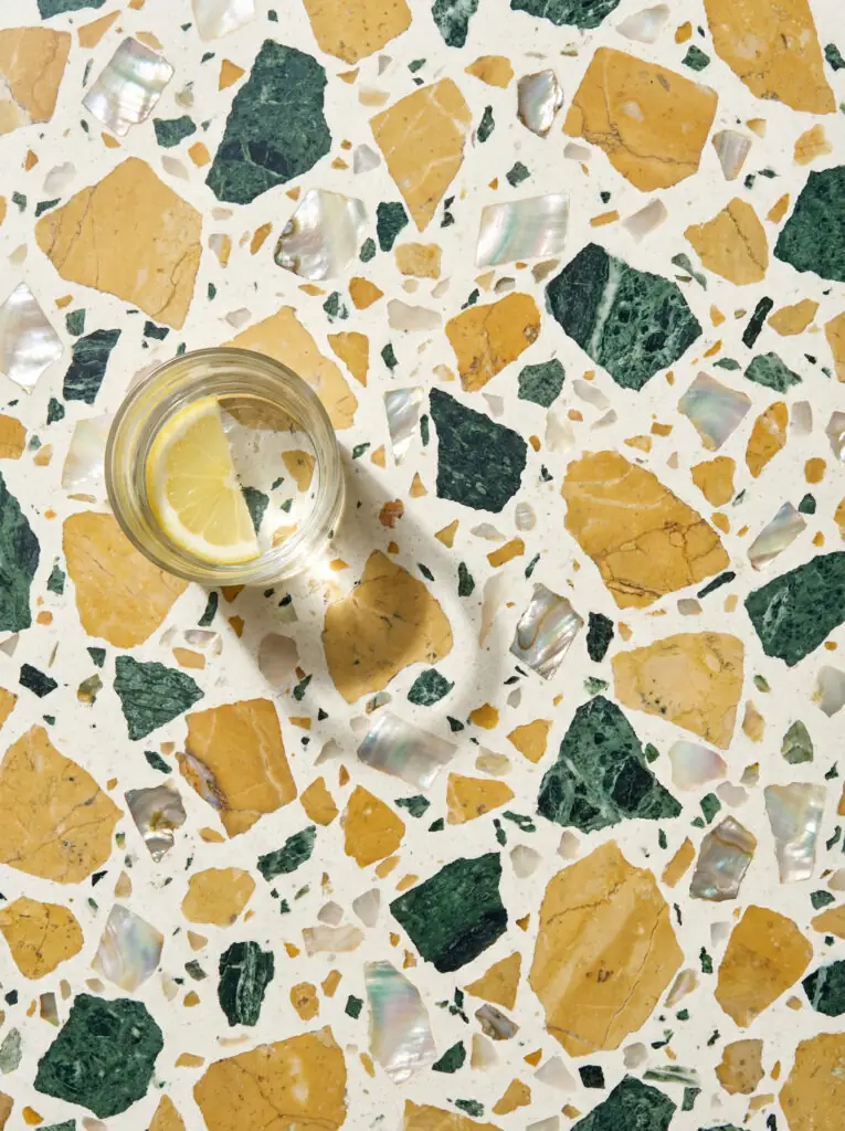 Gros plan macro de la texture d'un comptoir en terrazzo montrant de gros éclats de marbre vert, jaune et terracotta sur un fond blanc.