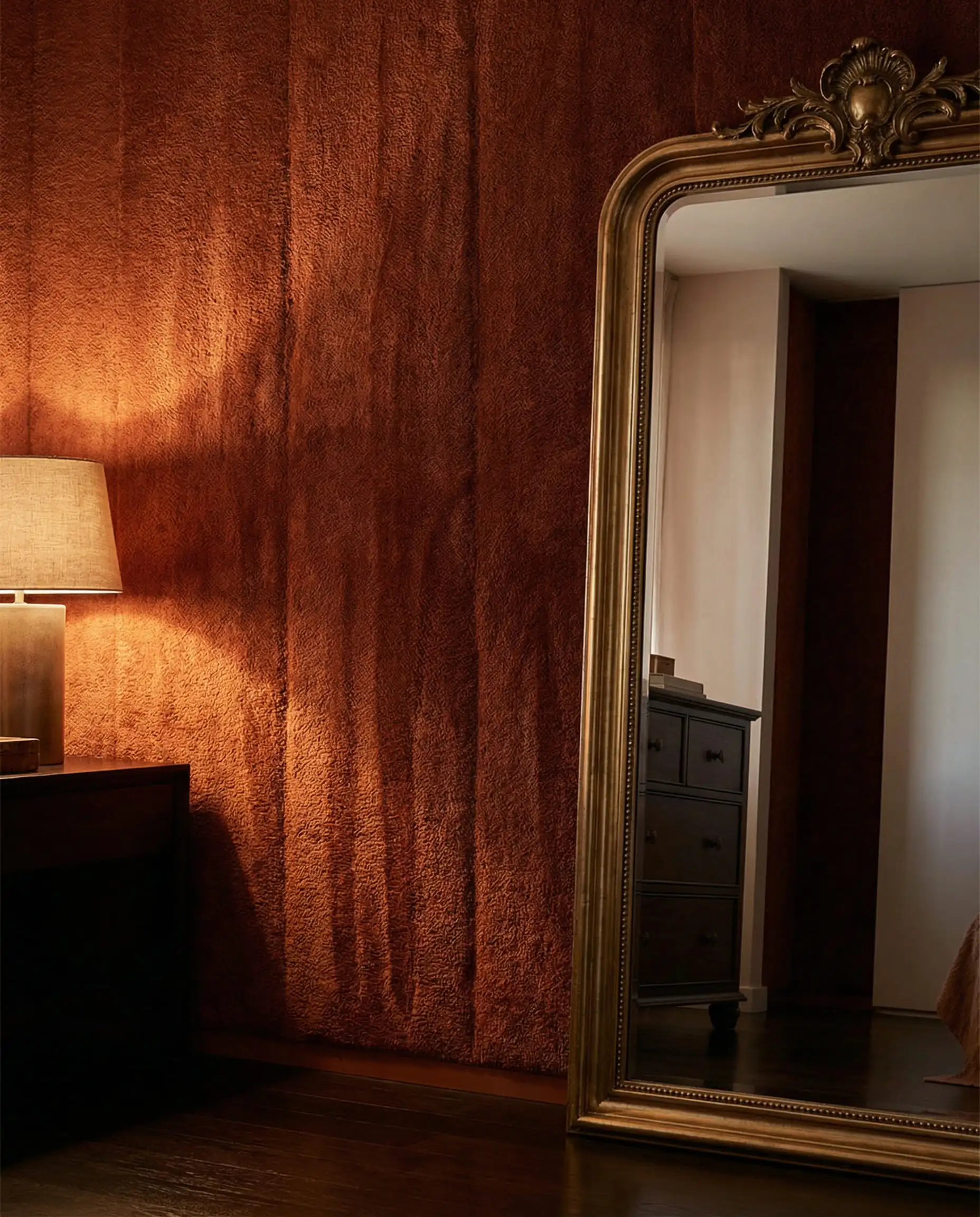 A luxurious bedroom accent wall completely covered in a heavy, rich bouclé velvet textile wallpaper in a deep, burnt orange/terracotta color. This bedroom features Deep terracotta, opulent gold, and dark wood floor tones and a opulent, cocooning, hotel vibe atmosphere.