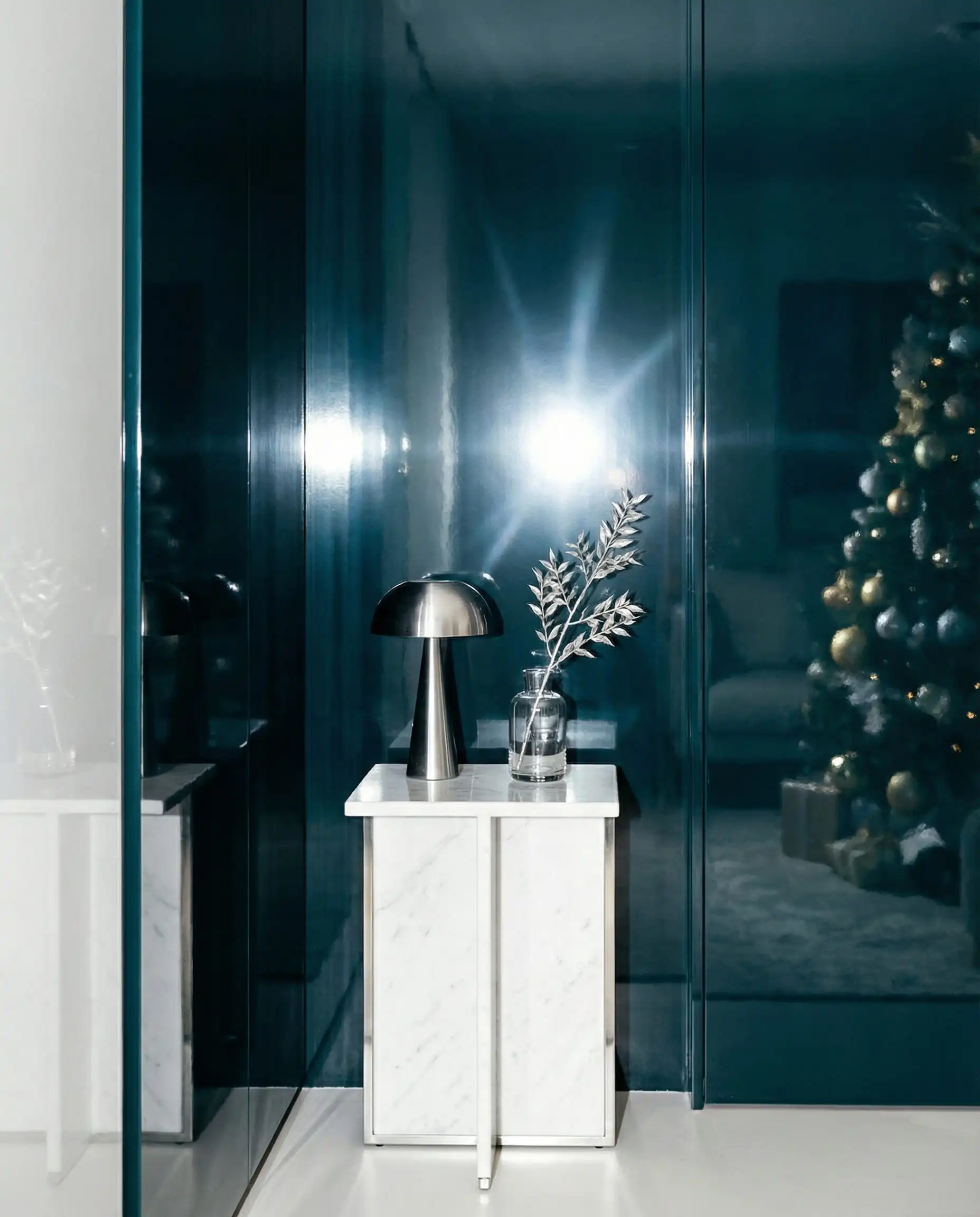 A living room featuring a statement wall painted in a dark, glossy, lacquered teal finish. This living room features High-gloss dark teal, pure white marble, and minimal silver accents tones and a dramatic, high-gloss, festive atmosphere.