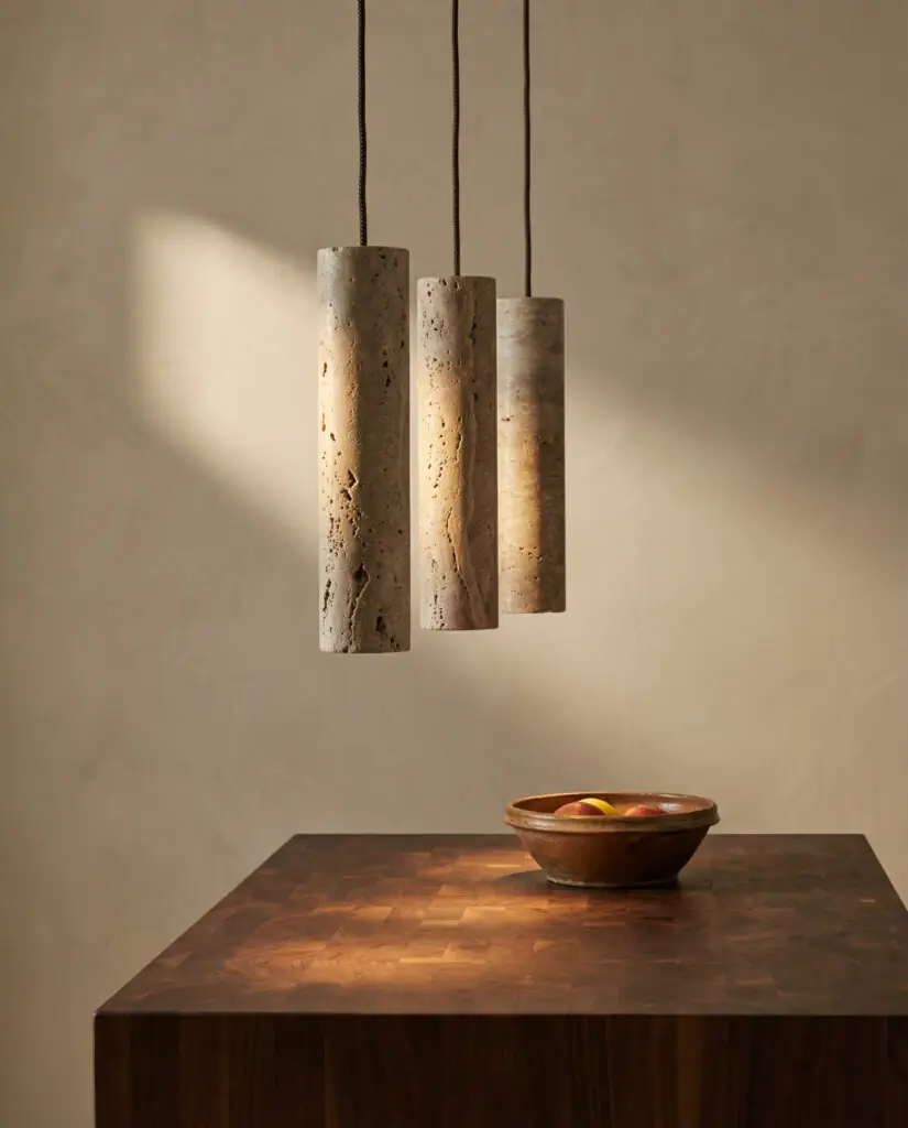 Three slender travertine cylinder pendants hang over a walnut butcher block counter against a limewash wall.