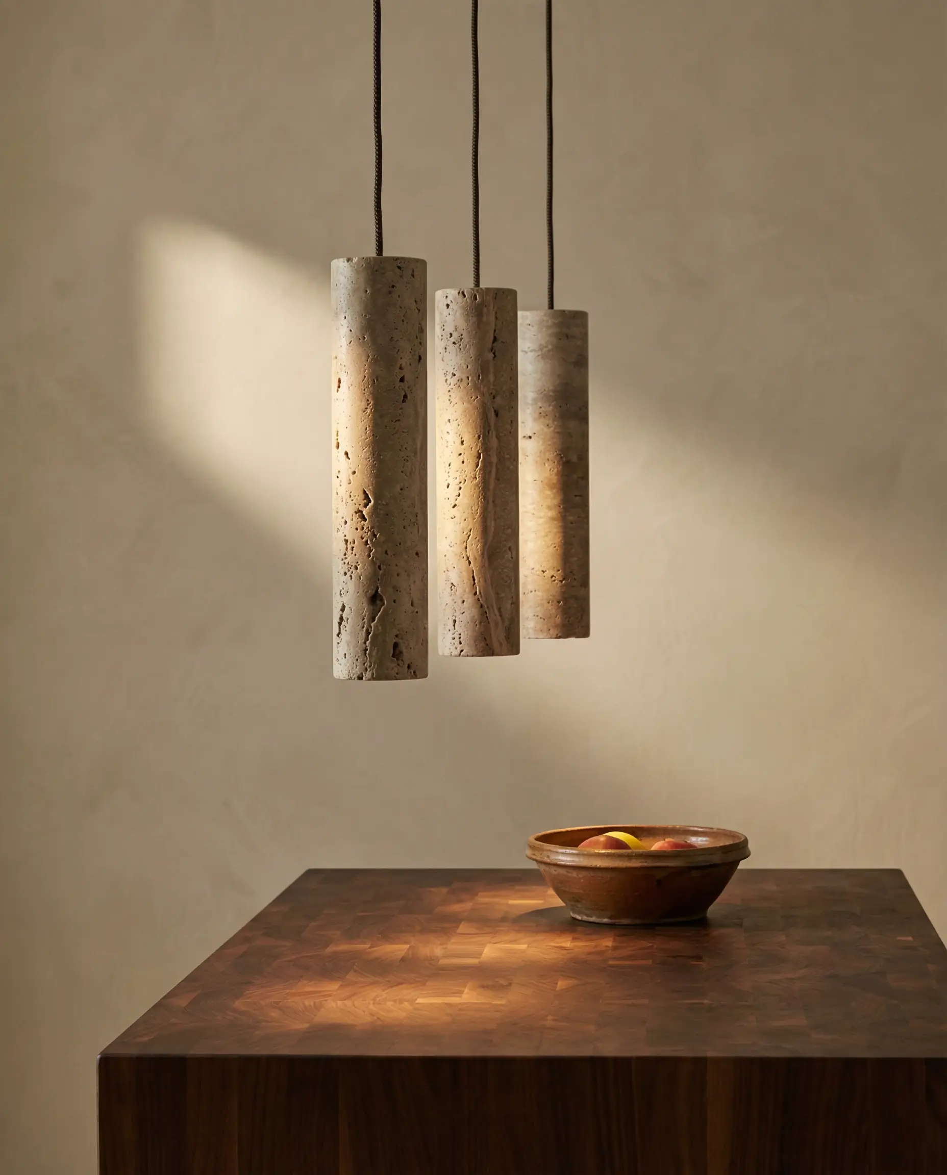 Three slender travertine cylinder pendants hang over a walnut butcher block counter against a limewash wall.