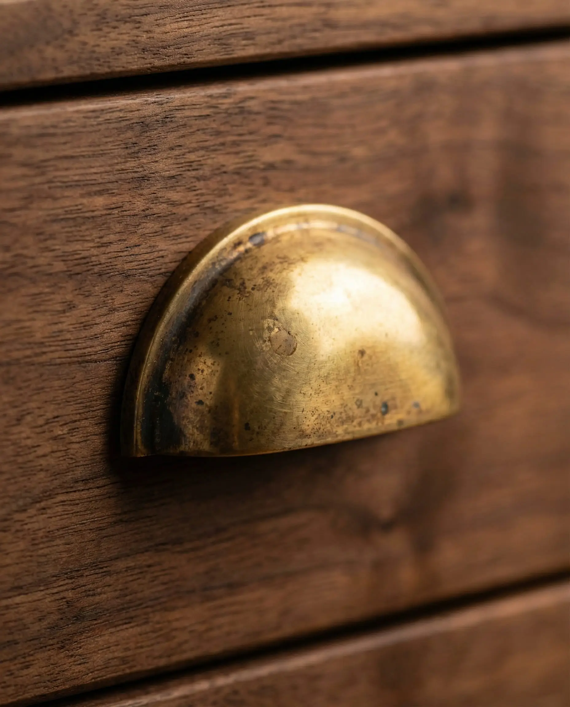 Detail shot of unlacquered brass cup pull on dark walnut drawer showing natural aging and patina.