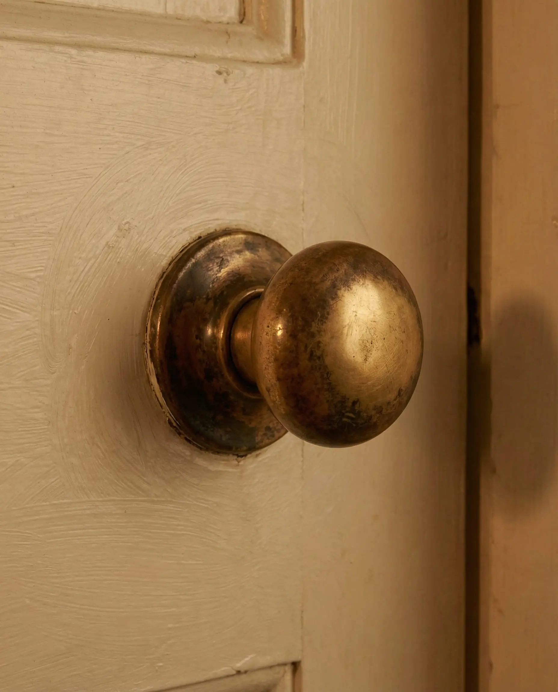Close-up of an unlacquered brass door knob with natural patina on a cream colored door.