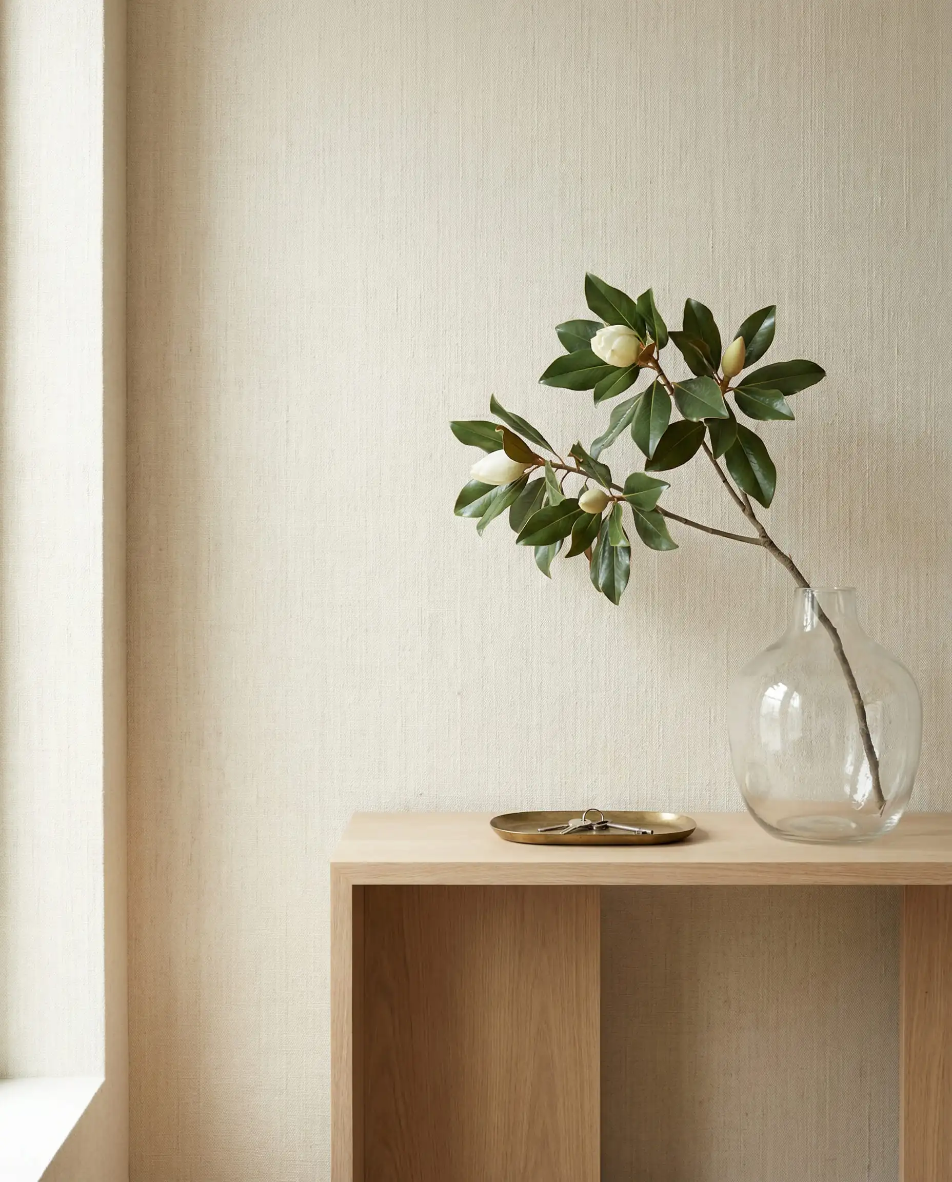 Minimalist living room wall featuring heavy woven linen wallpaper in a soft oatmeal color styled with a white oak console.