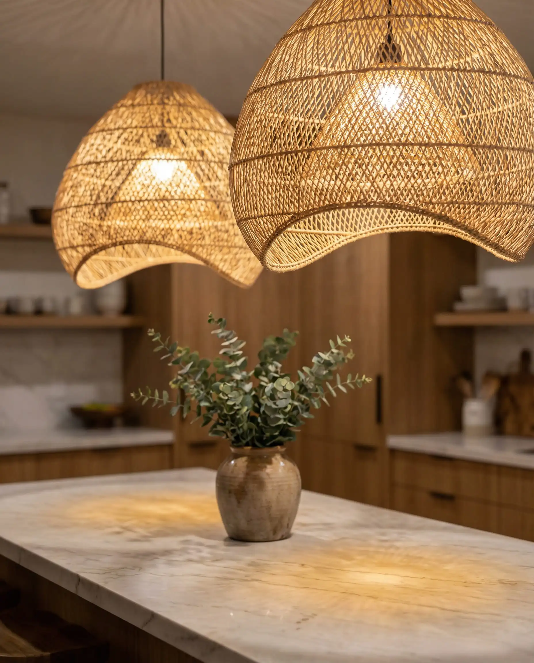 Two large woven rattan pendant lights hanging over a marble kitchen island countertop.