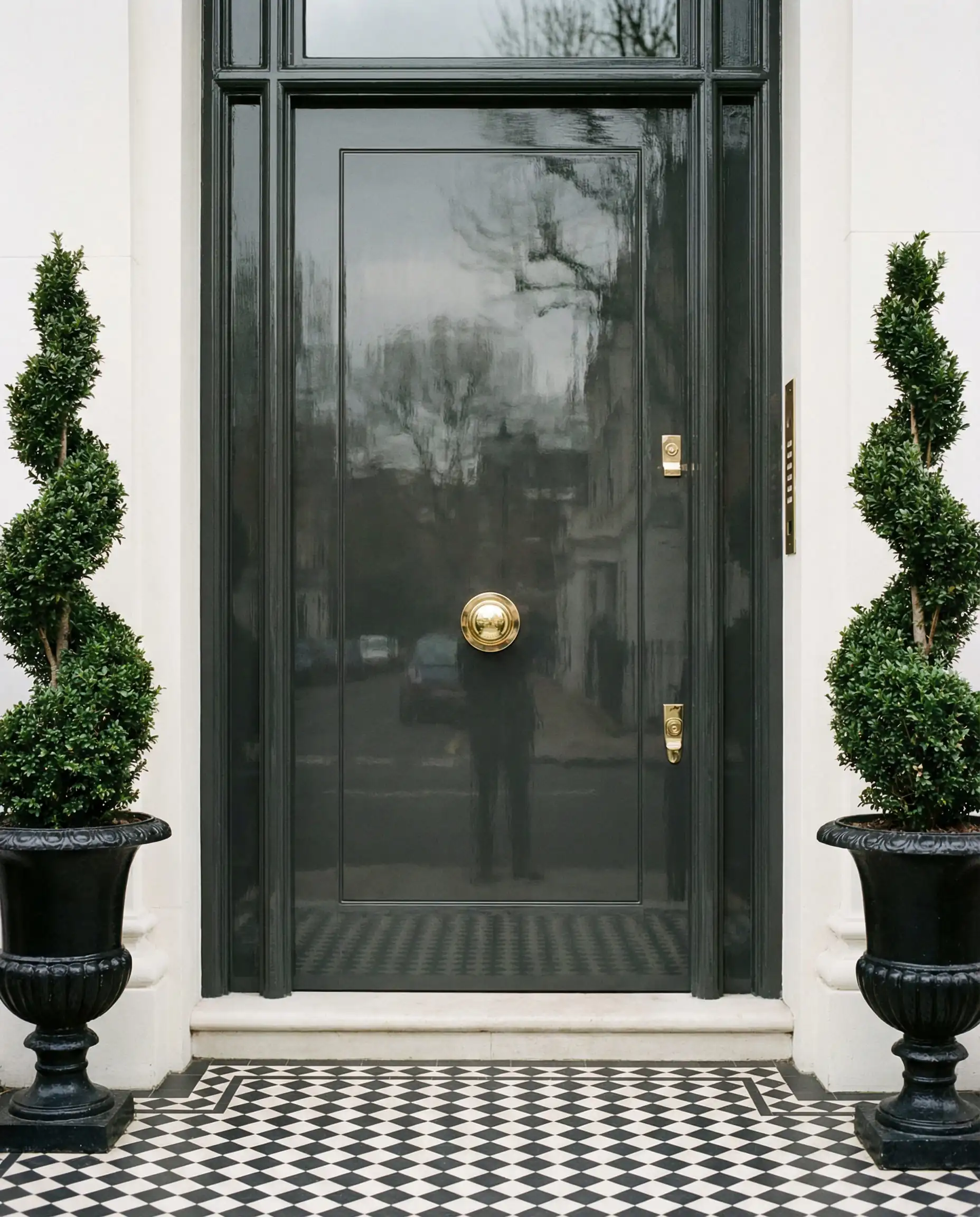 Luxurious London-style front entrance featuring a high-gloss Behr Black door with polished brass hardware and topiary trees.