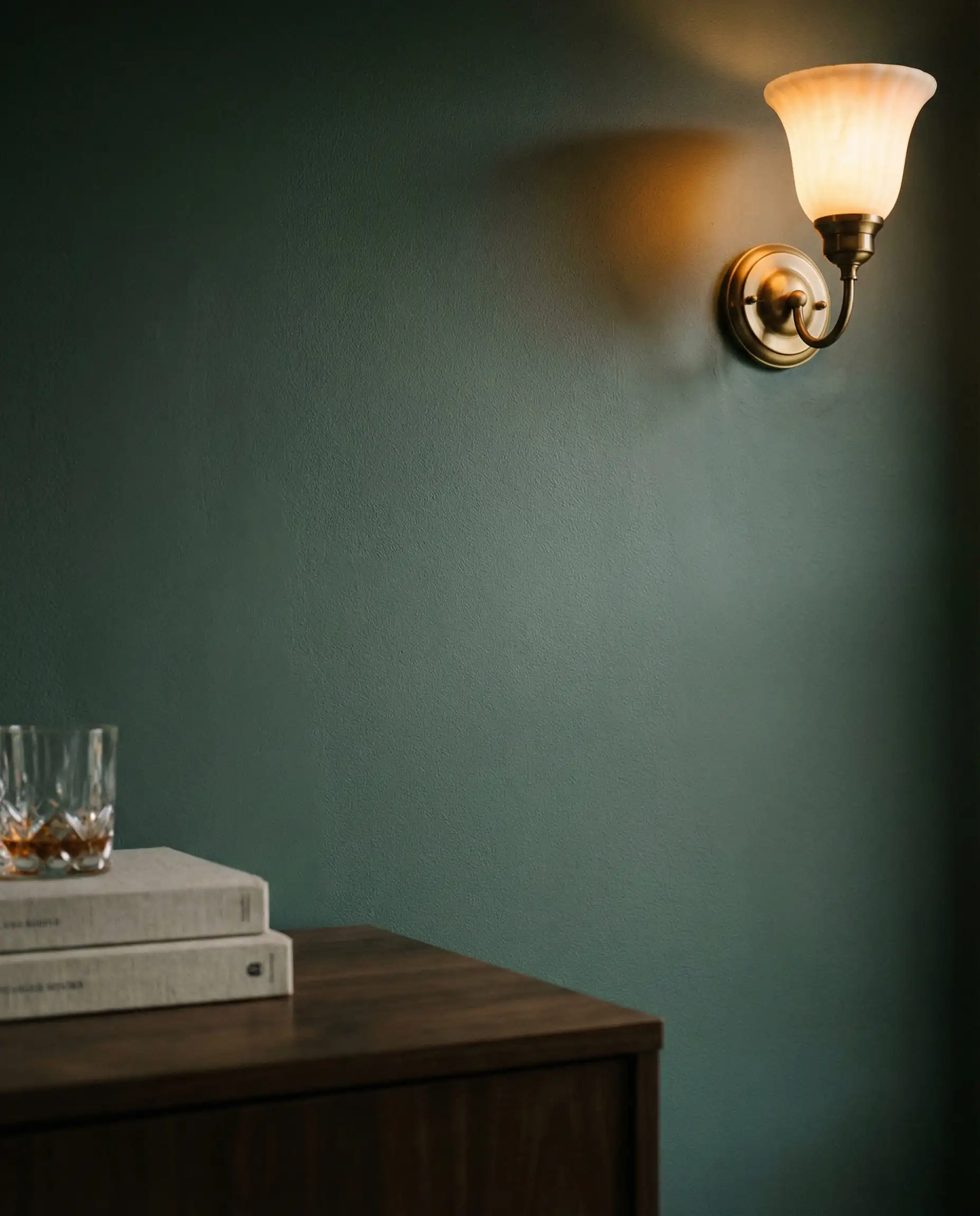 Close up of Behr Hidden Gem green paint texture on a wall with antique brass sconce lighting.